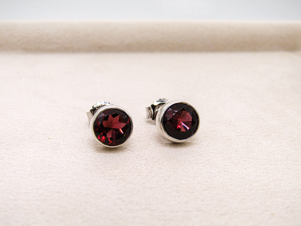 Pair of silver stud earrings with red gemstones on a light beige background