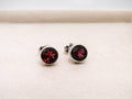 Pair of silver stud earrings with red gemstones on a light beige background