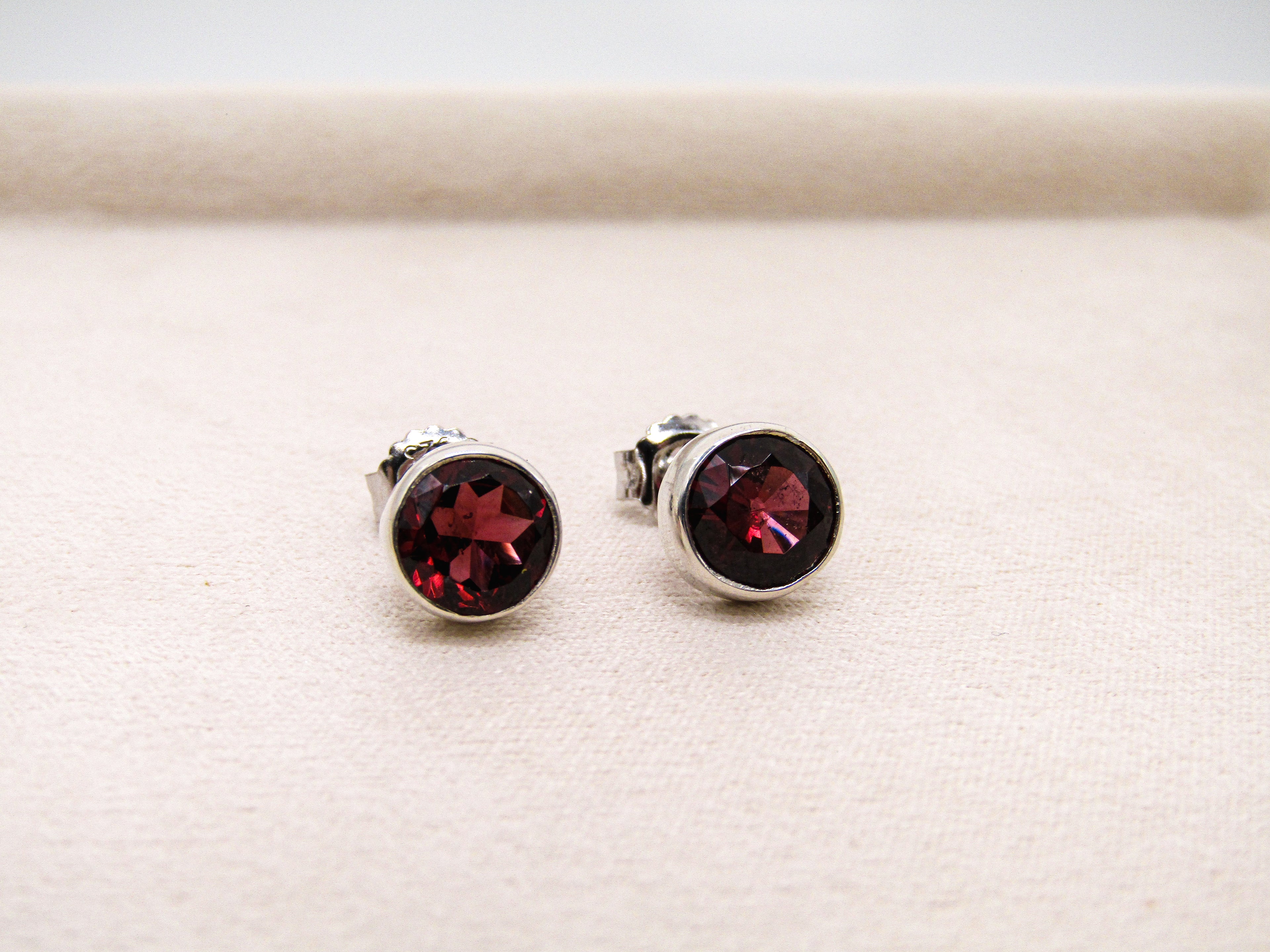 Pair of silver stud earrings with red gemstones on a light beige background