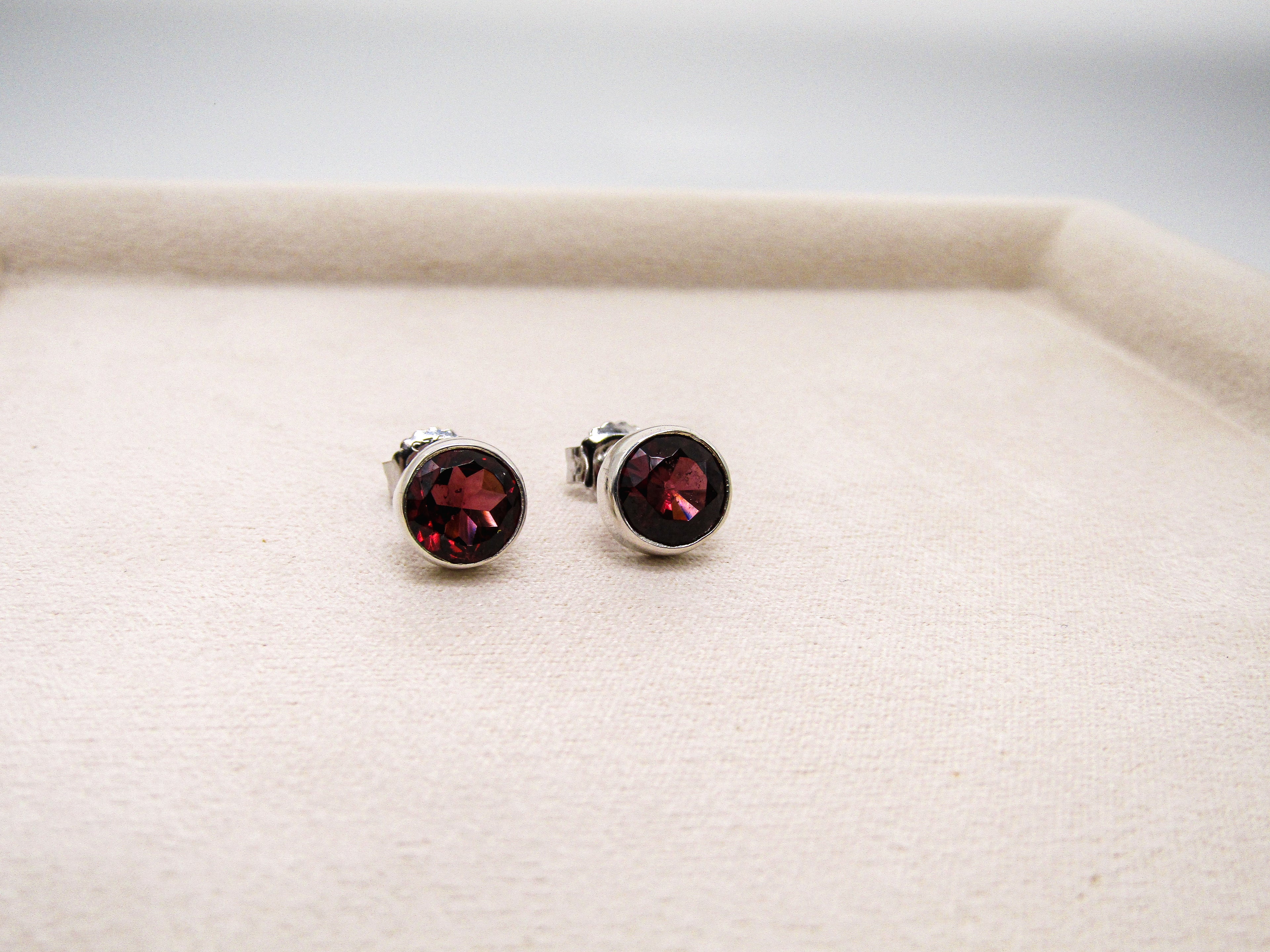 Pair of silver earrings with red gemstones on a beige surface