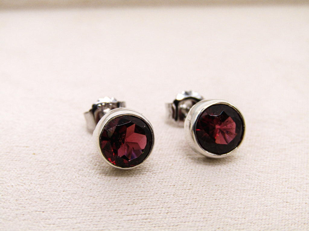 Pair of silver stud earrings with red gemstones on a light beige background
