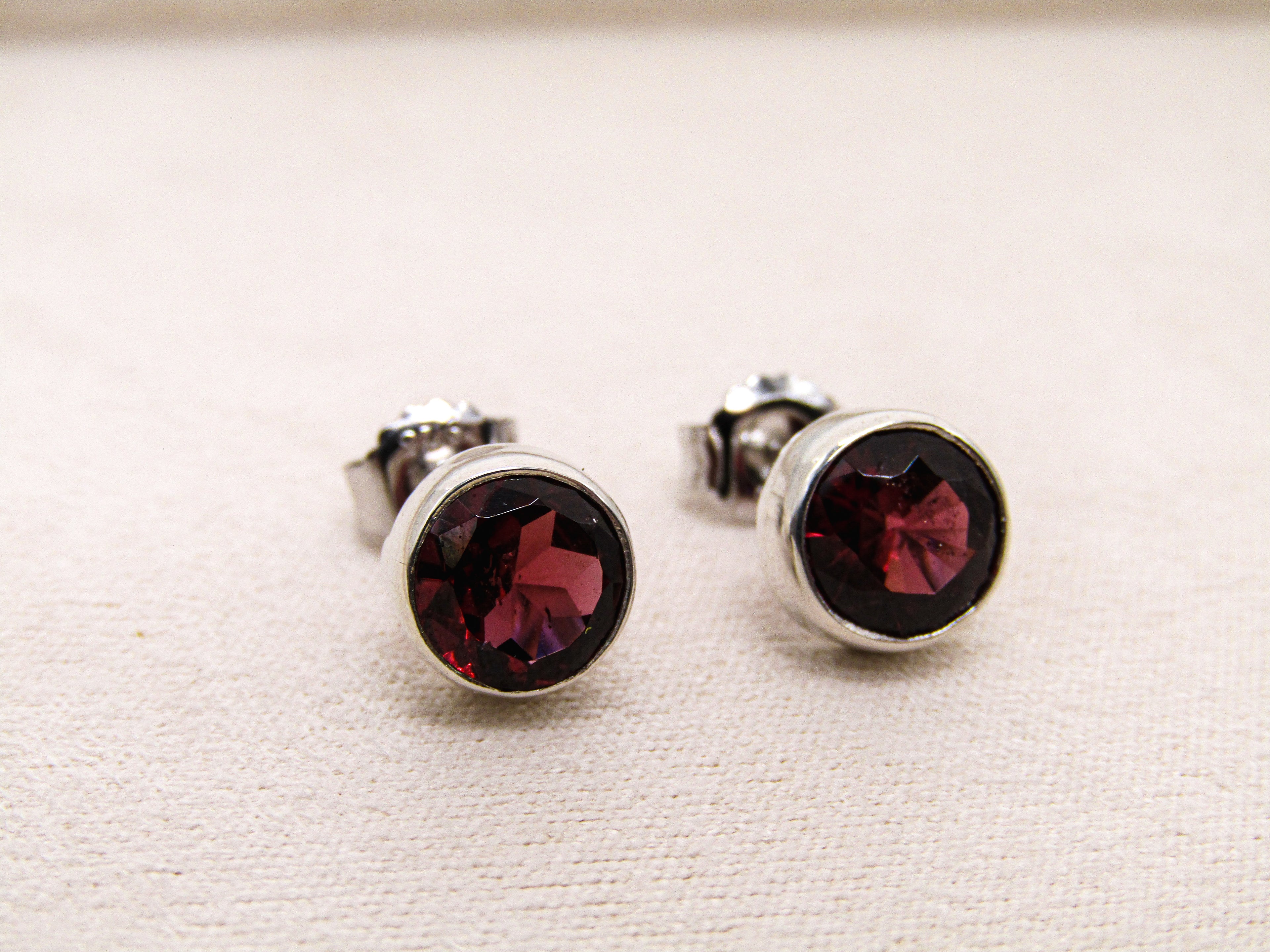 Pair of silver stud earrings with red gemstones on a light beige background