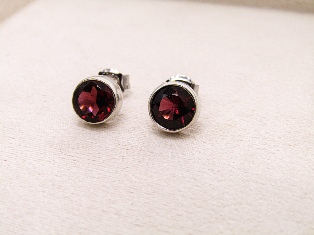 Pair of silver stud earrings with red gemstones on a white fabric background