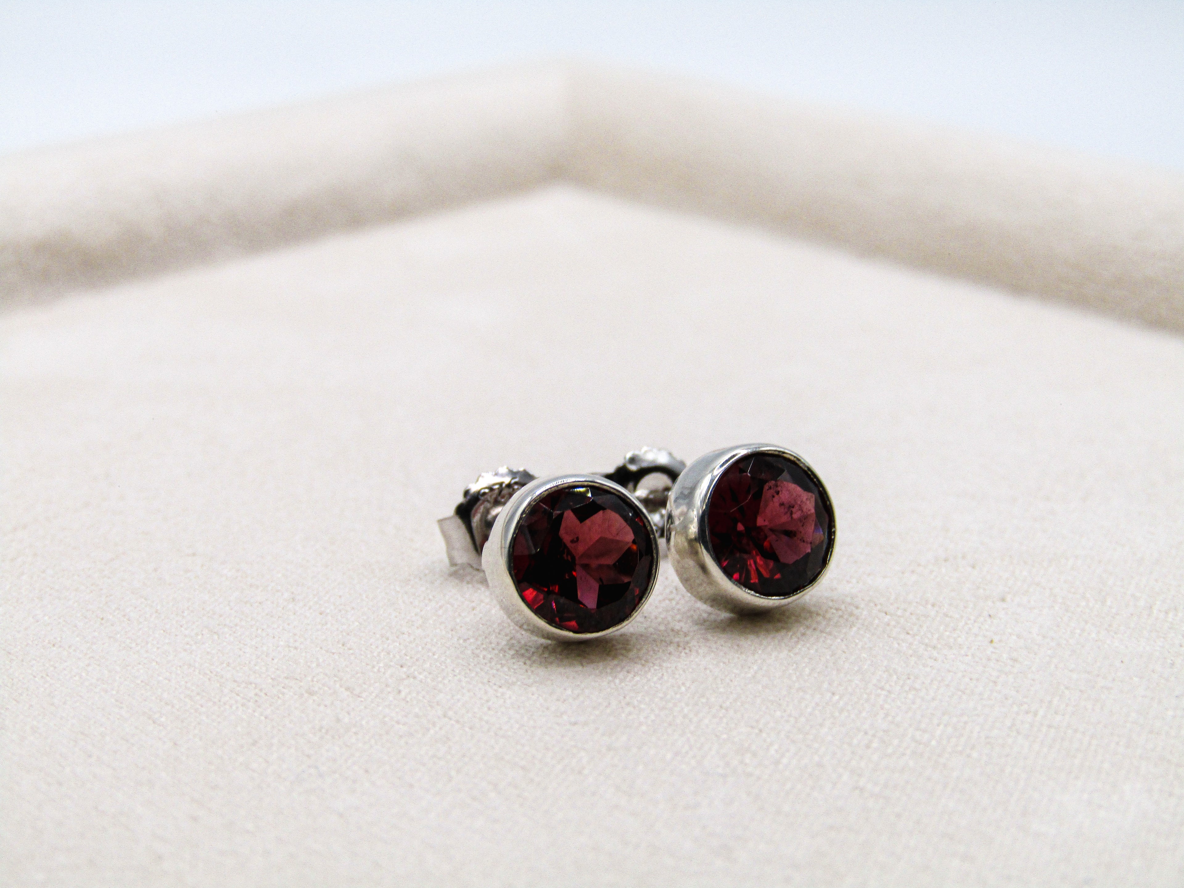 Pair of silver stud earrings with red gemstones on a white background