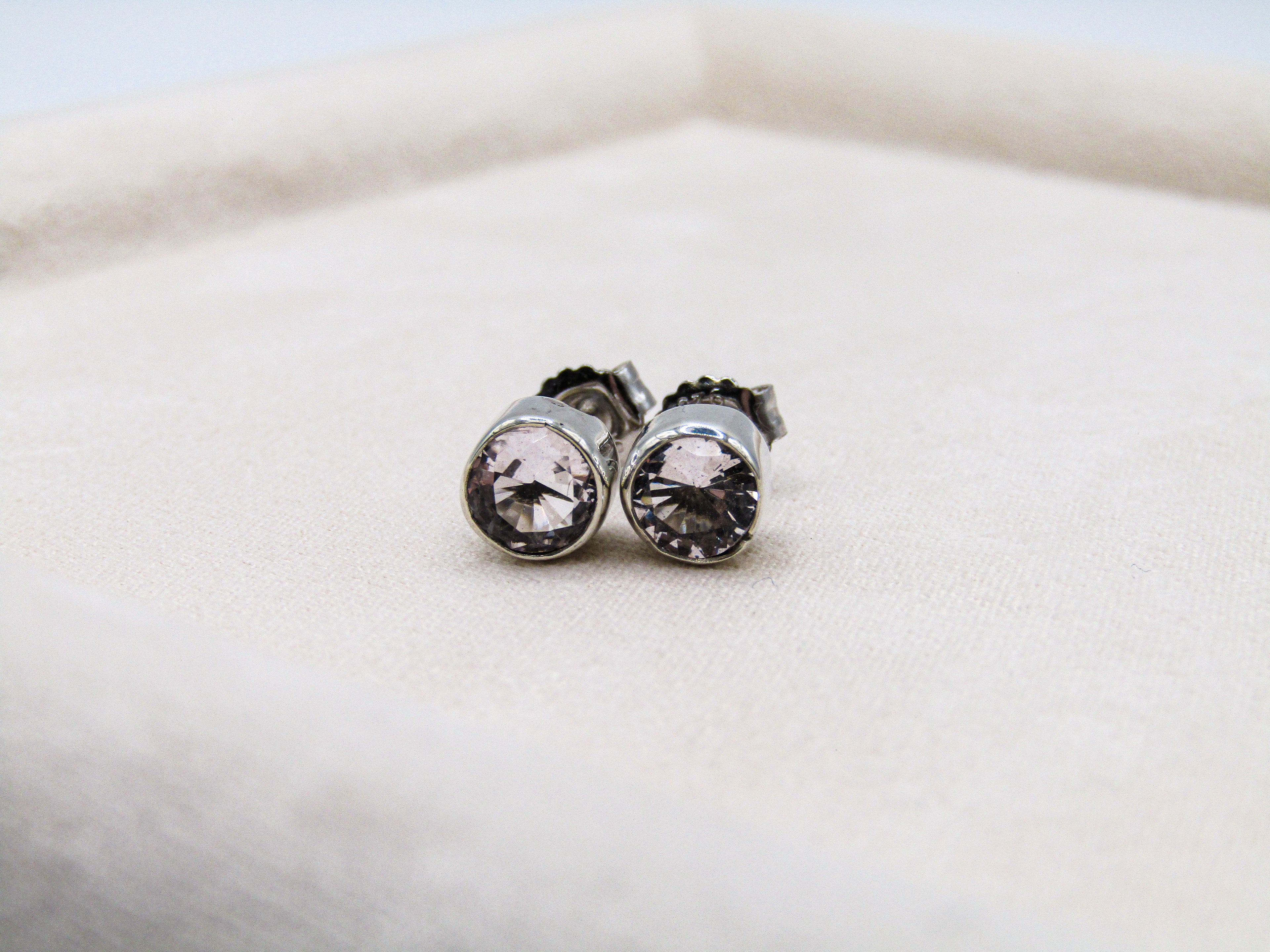 Pair of silver earrings with clear gemstones on a white cushion