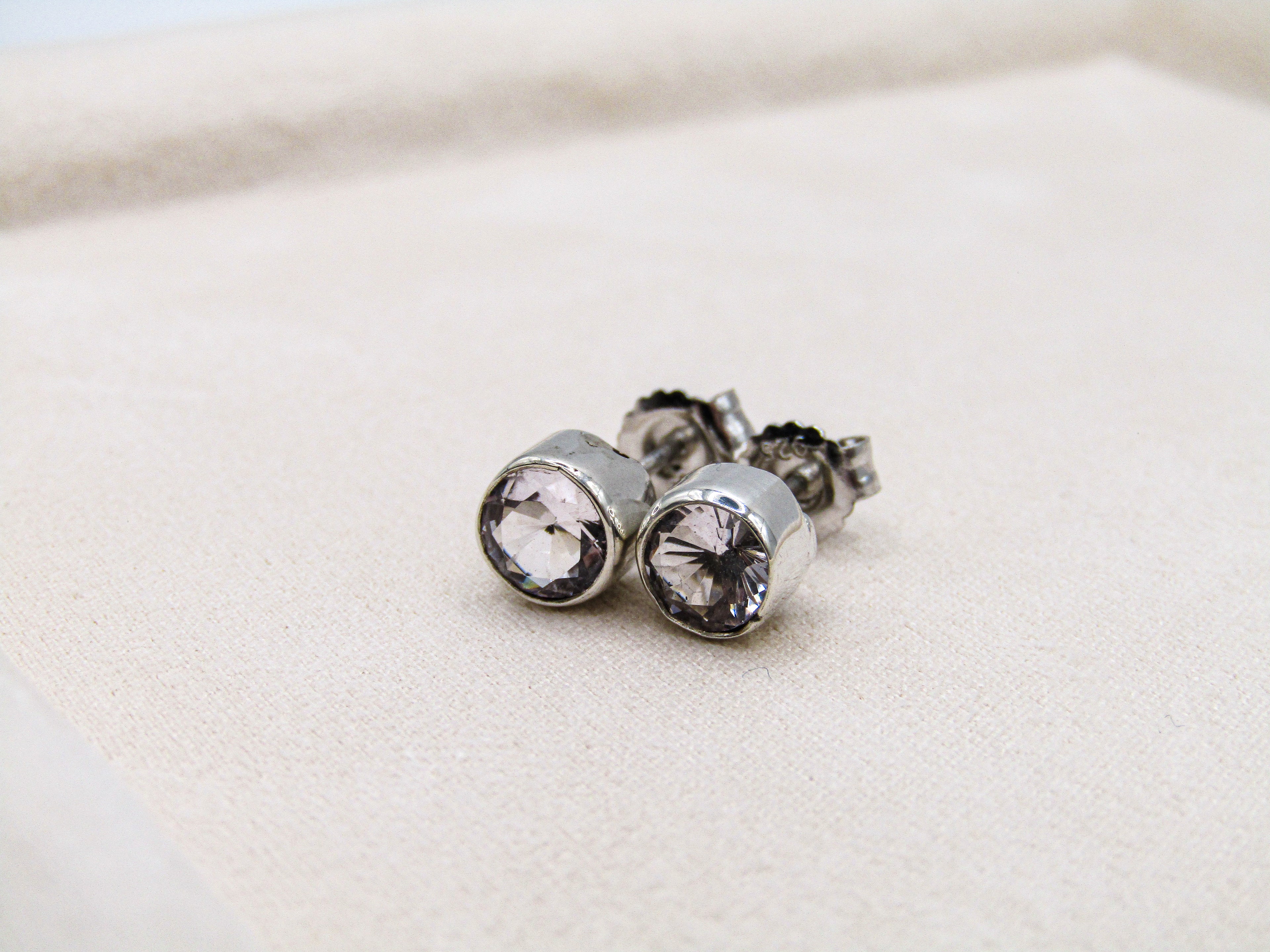 Silver stud earrings with clear gemstones on a light beige background