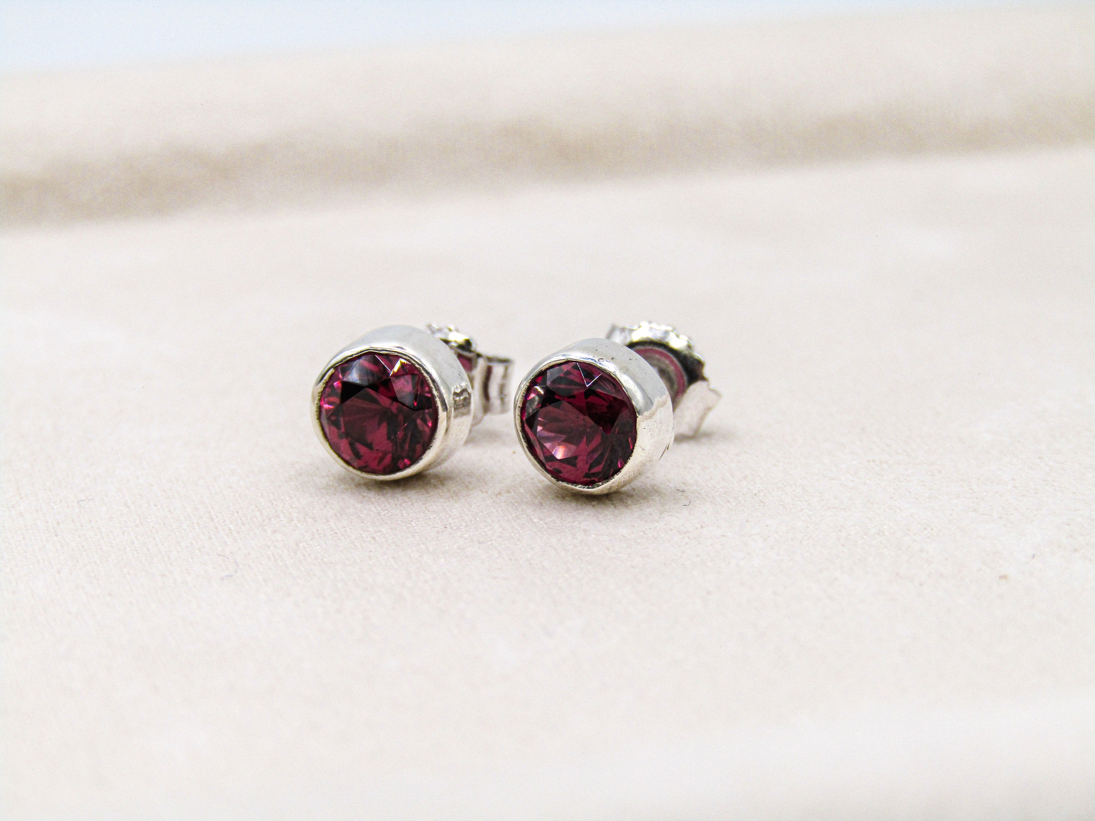 Silver stud earrings with red gemstones on a light background