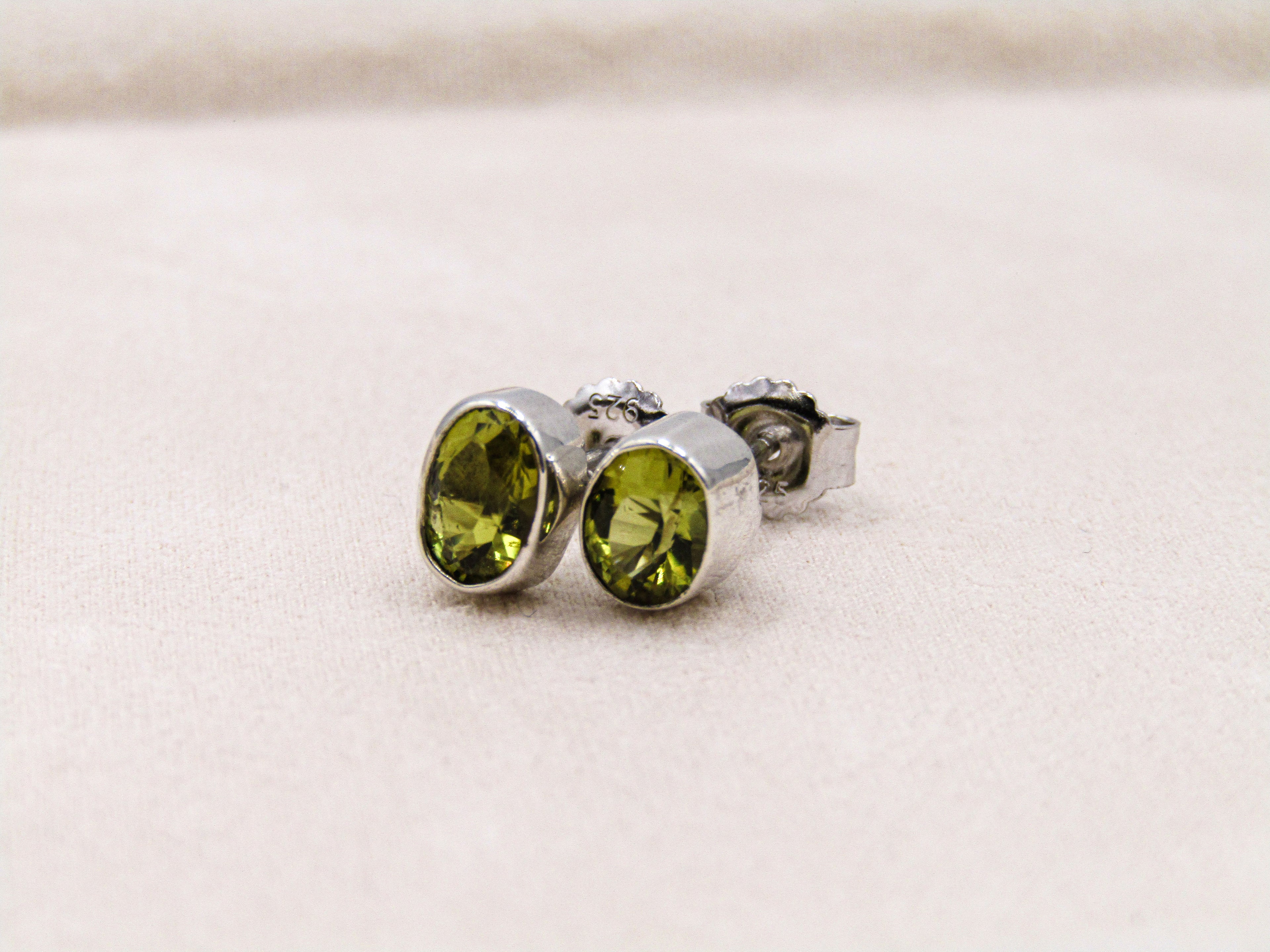 Silver stud earrings with green gemstones on a light beige background