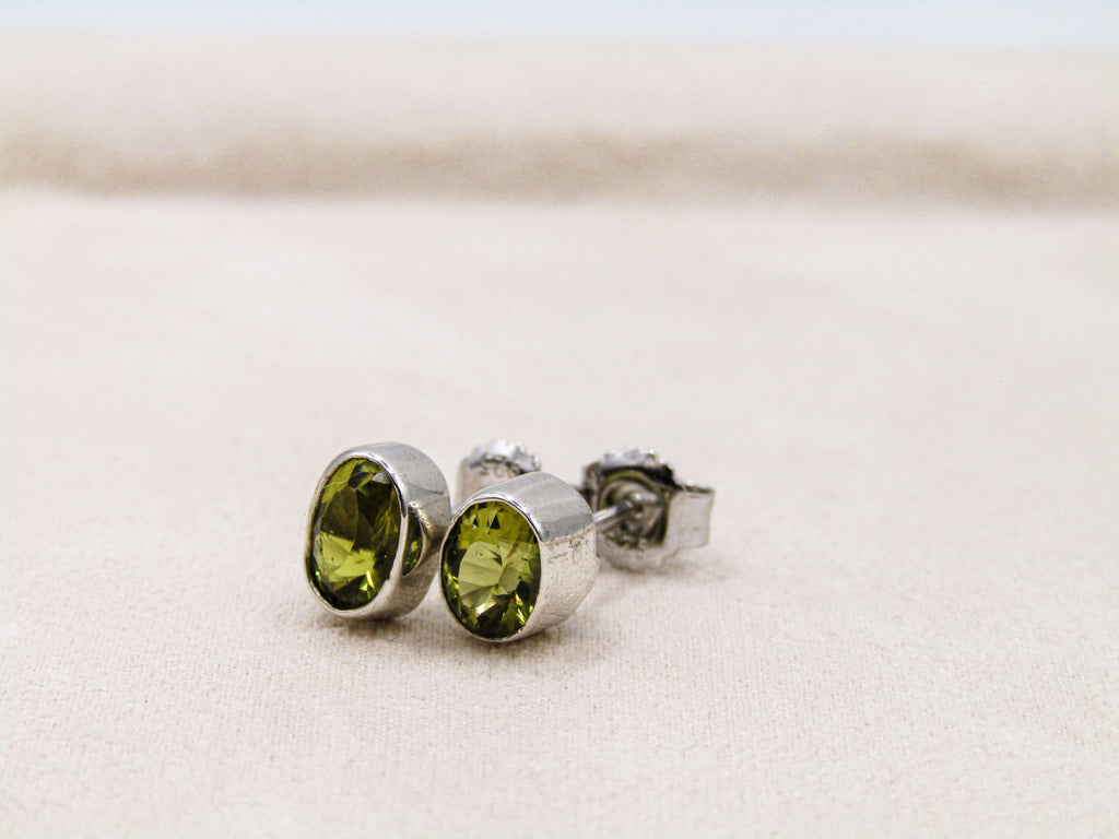 Silver earrings with green gemstones on a light beige background
