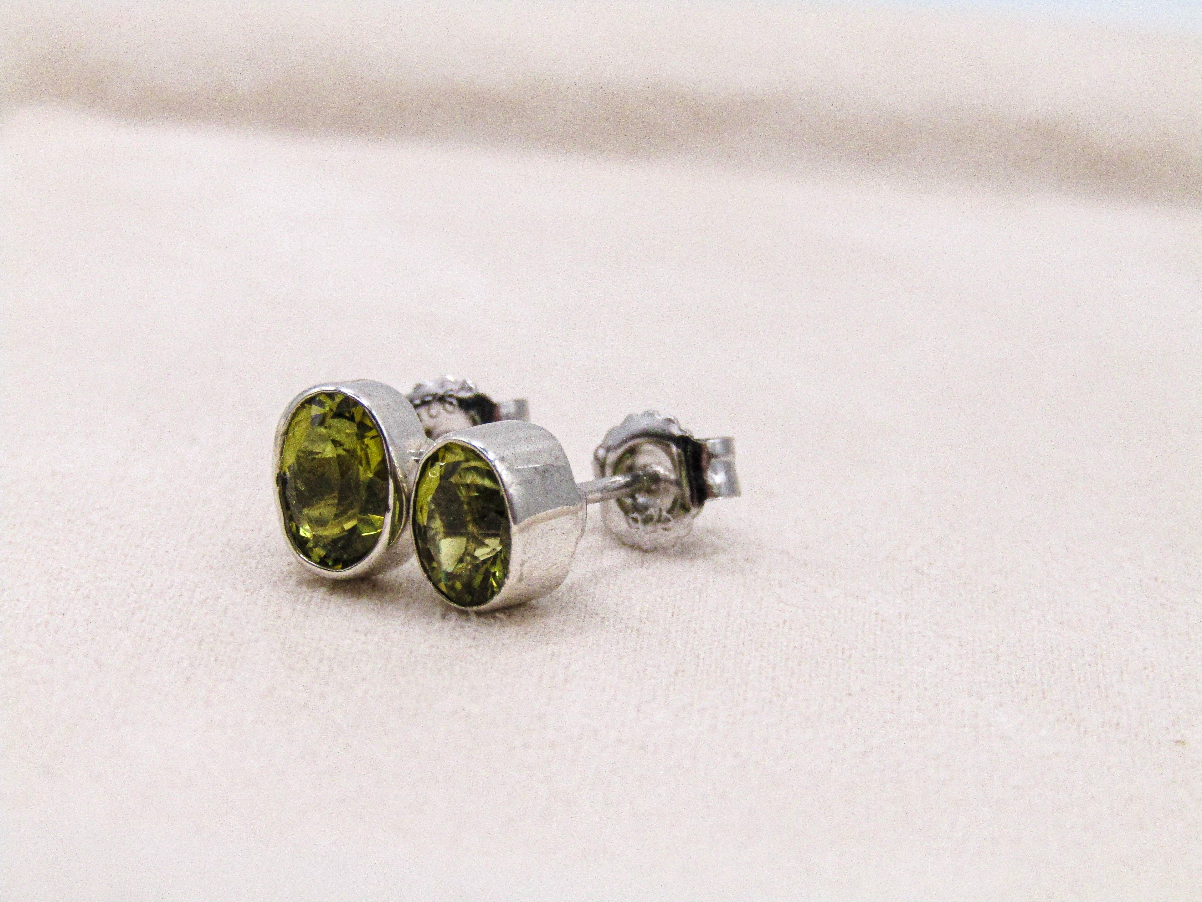 Silver earrings with green gemstones on a light beige background