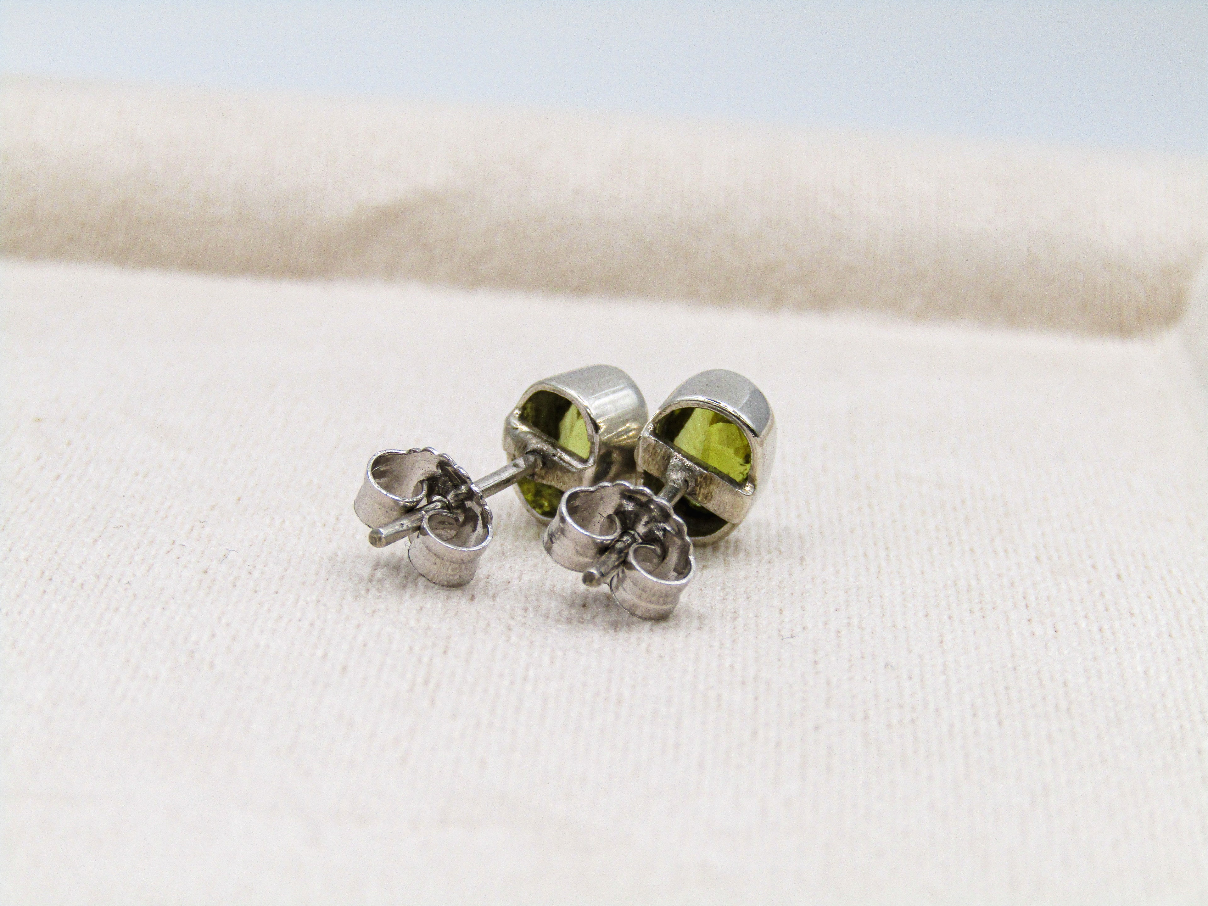 Silver earrings with green gemstones on a white fabric background