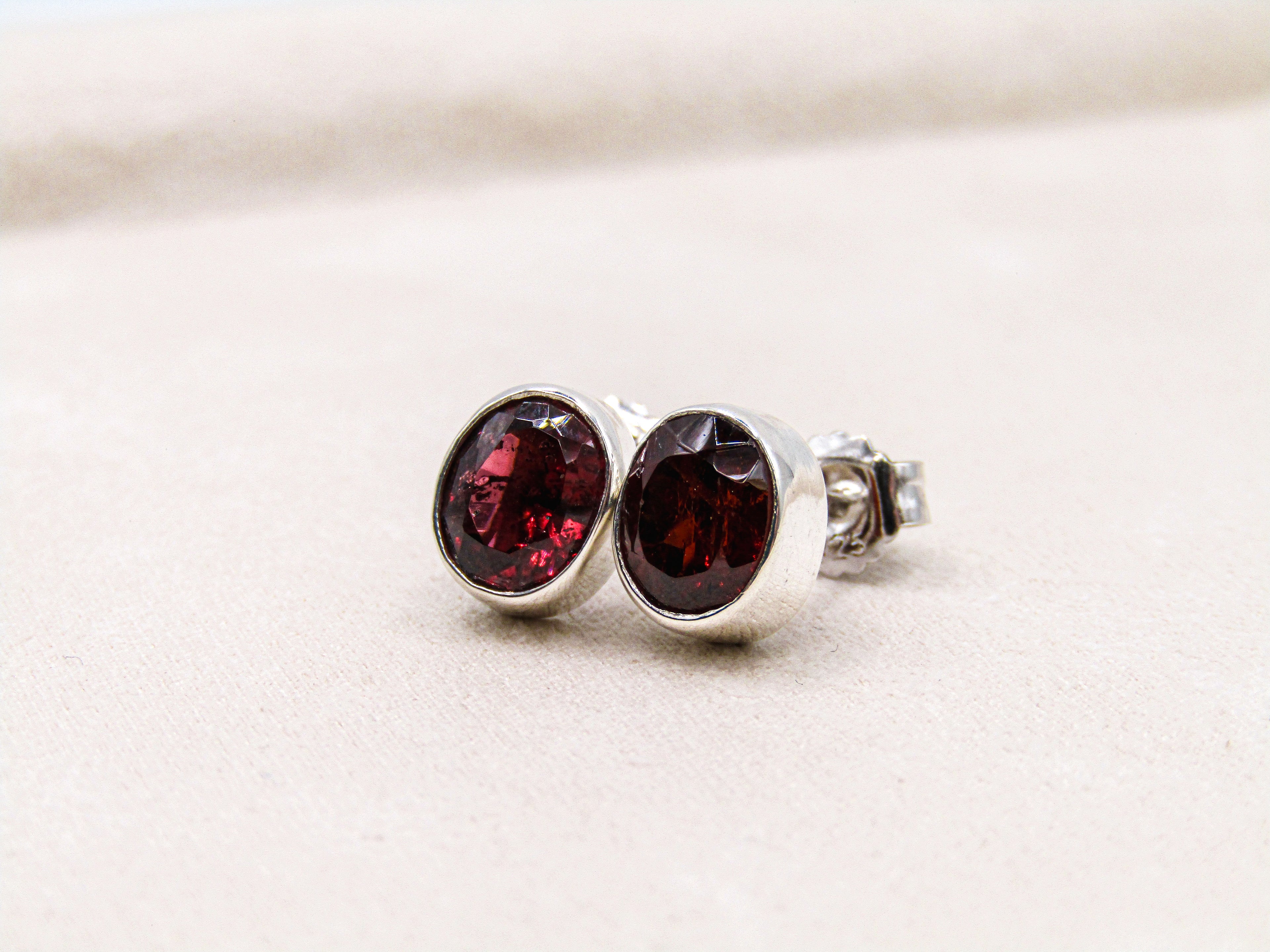 Silver earrings with red gemstones on a light beige background