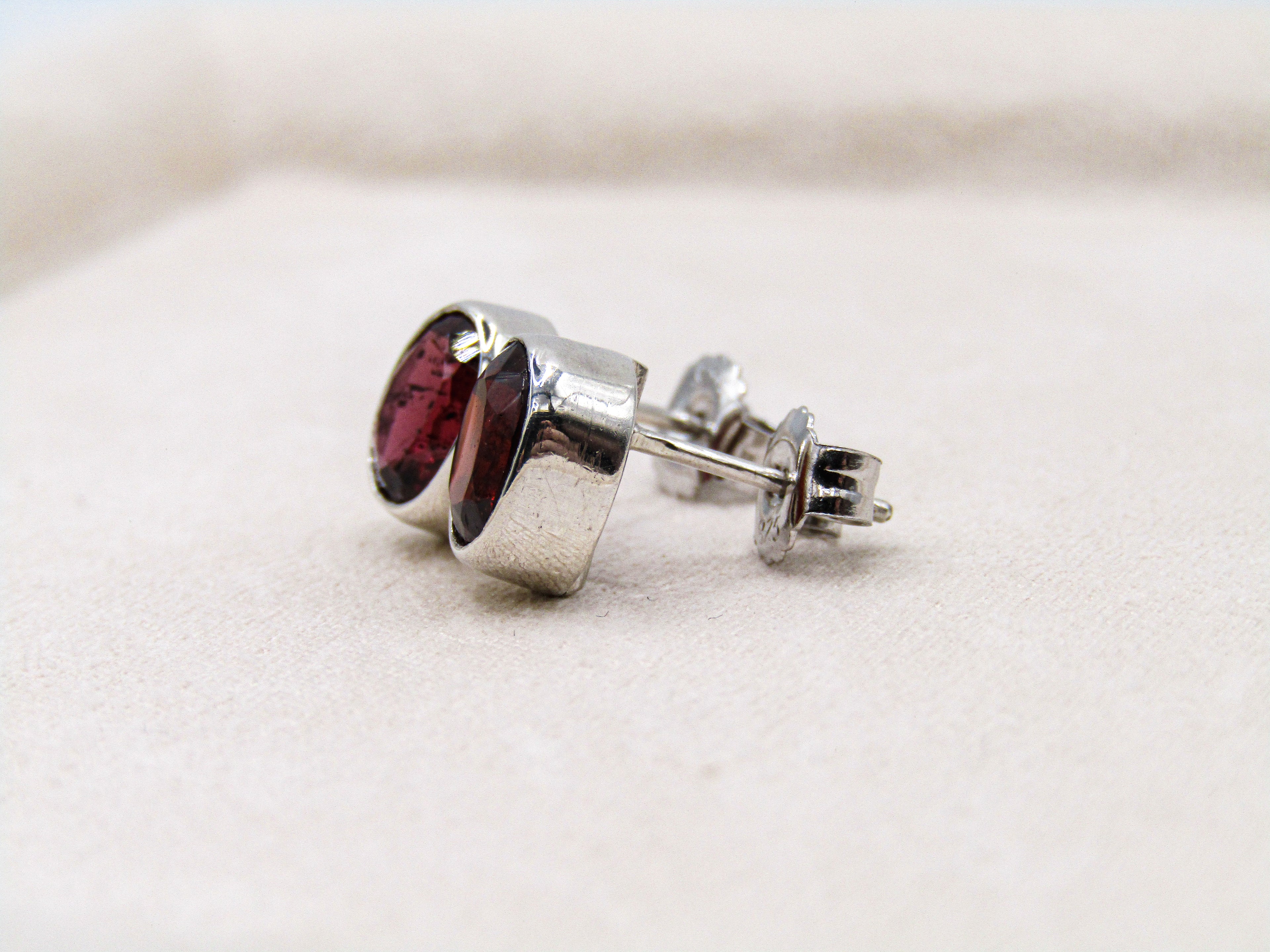 Silver earring with a red gemstone on a light background