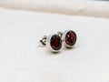 Pair of silver earrings with red gemstones on a white surface