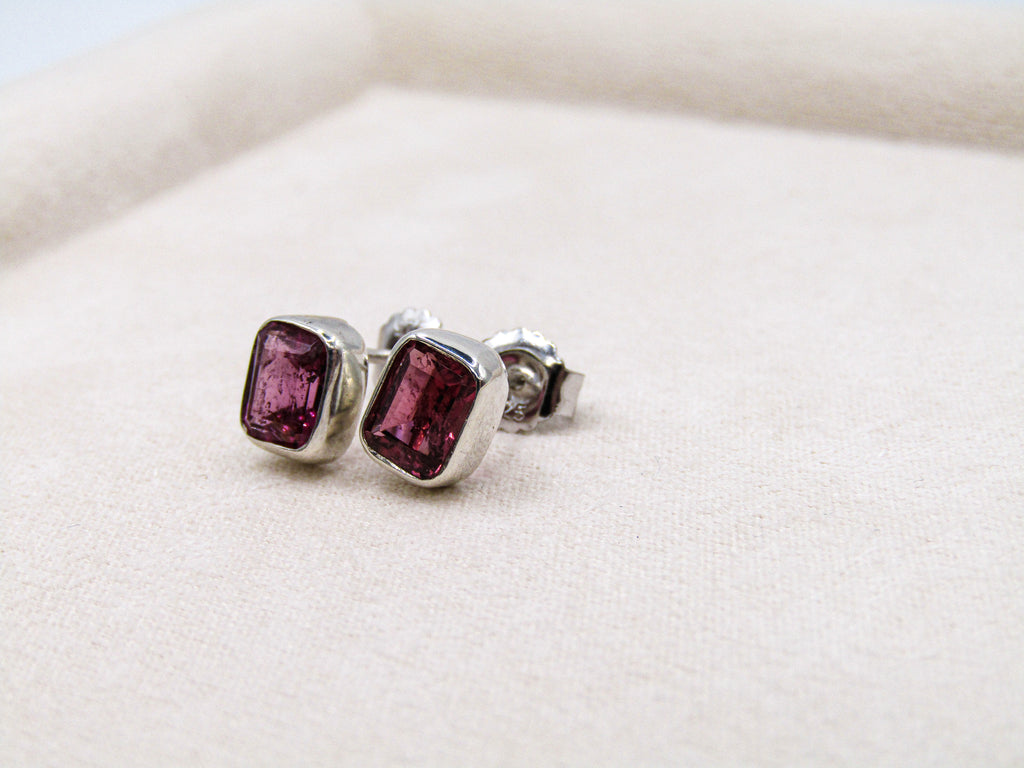 Pair of silver earrings with purple gemstones on a white background