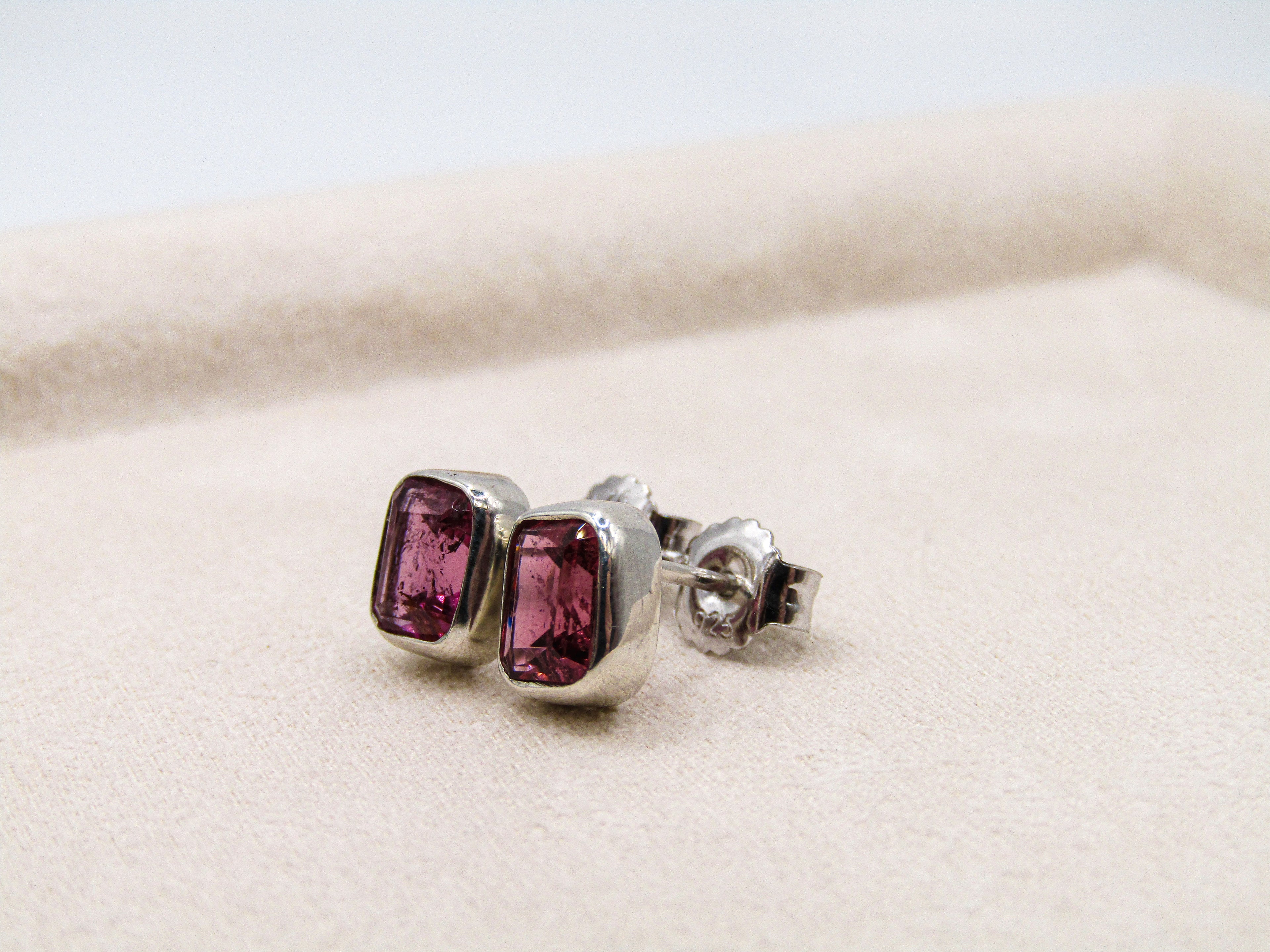 Pair of silver earrings with pink gemstones on a white background
