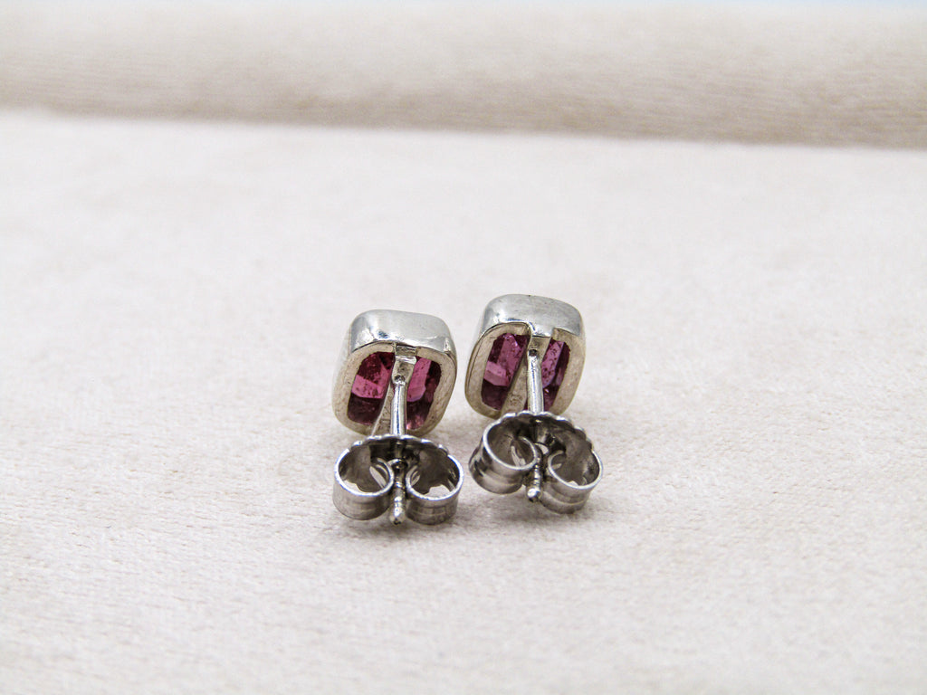 Pair of silver earrings with pink gemstones on a white fabric background