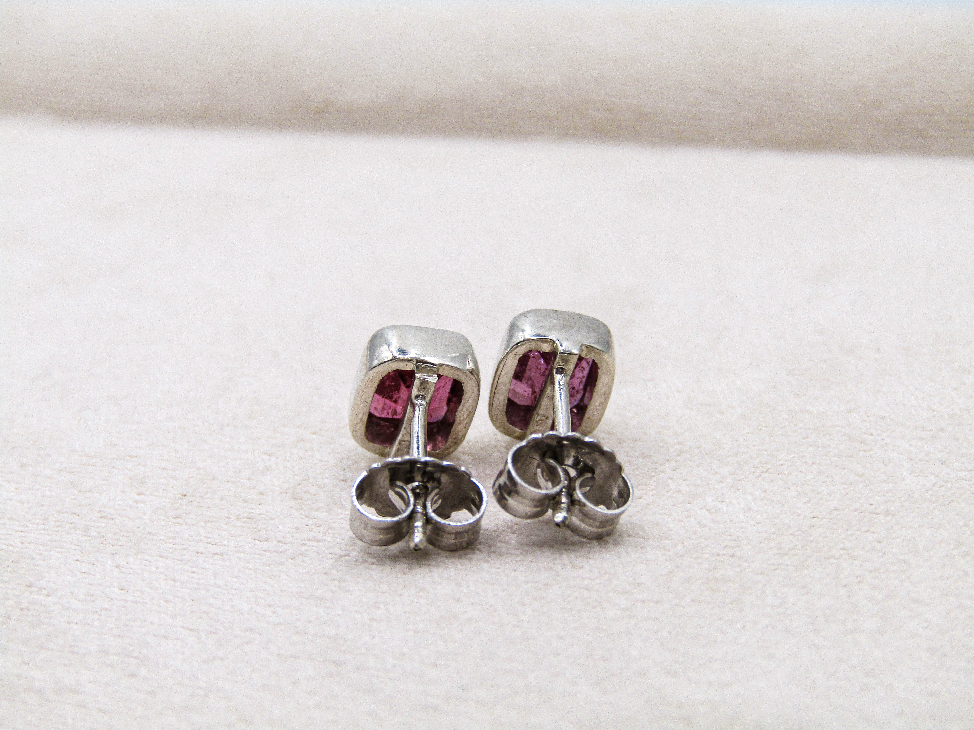 Pair of silver earrings with pink gemstones on a white fabric background