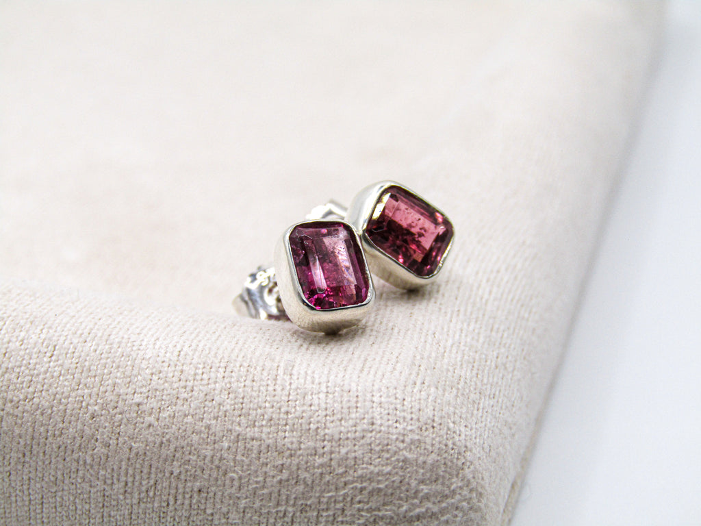 Silver earrings with pink gemstones on a beige fabric background