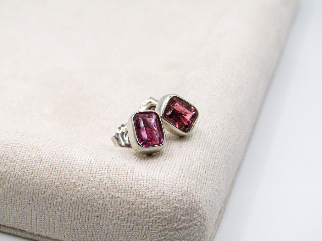 Pair of silver earrings with pink gemstones on a beige fabric background