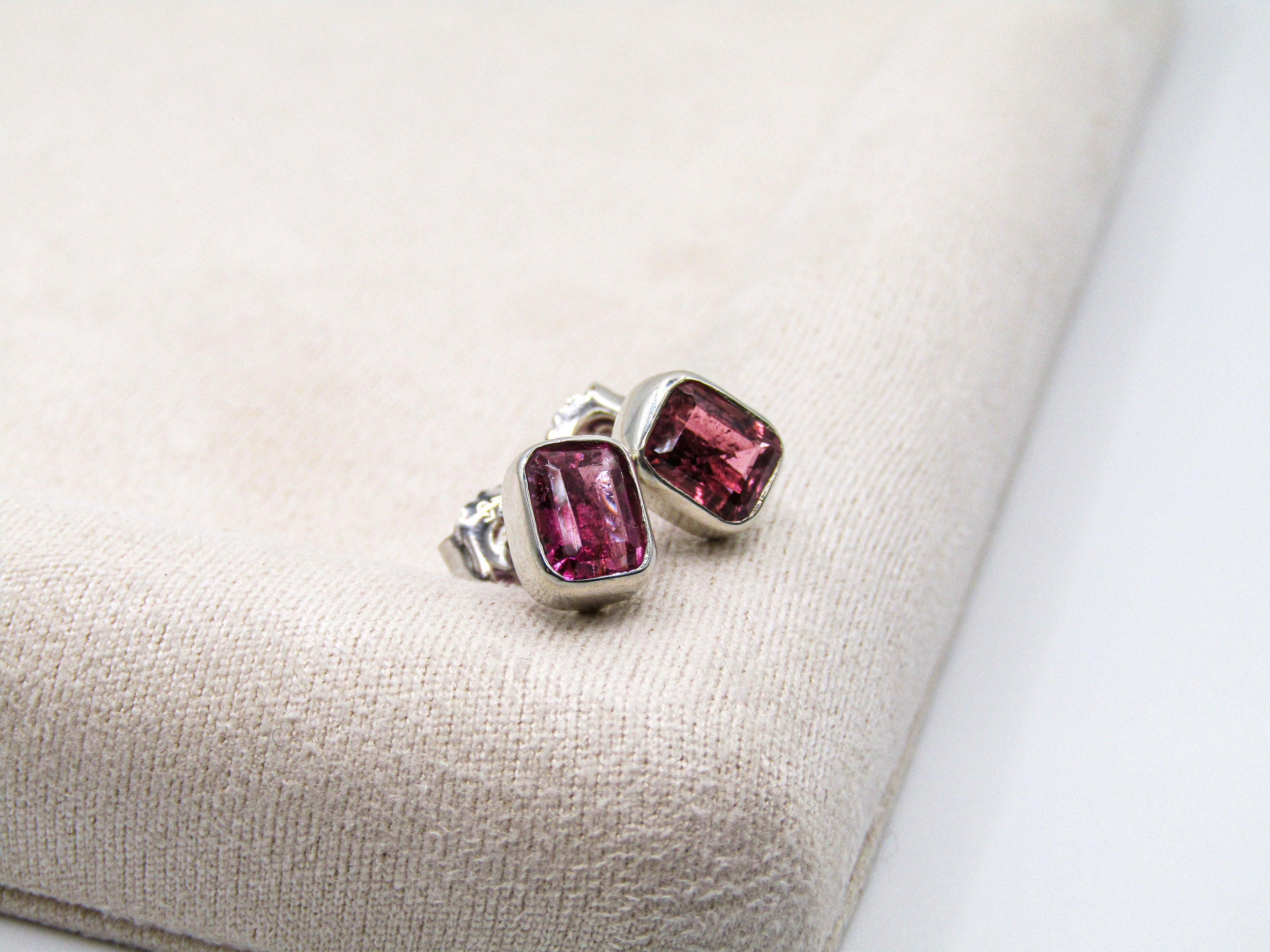 Pair of silver earrings with pink gemstones on a beige fabric background