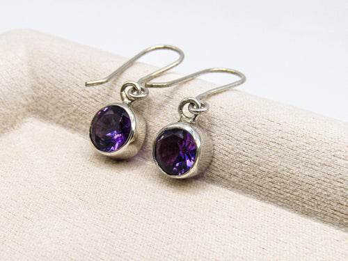 Silver earrings with purple gemstones on a beige fabric background