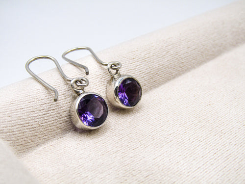 Silver earrings with purple gemstones on a white fabric background