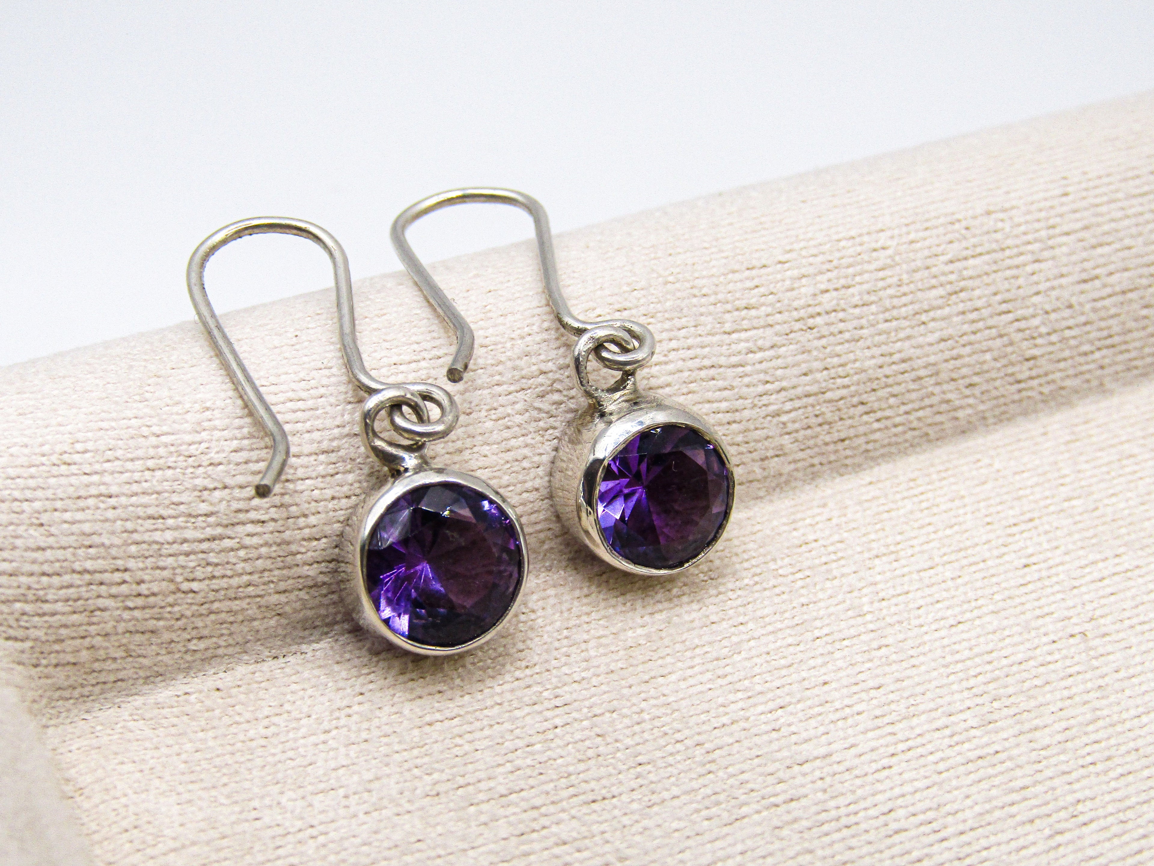 Pair of silver earrings with purple gemstones on a beige fabric background
