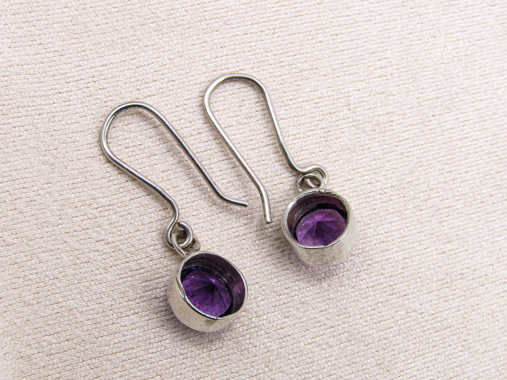 Silver earrings with purple gemstones on a textured white background