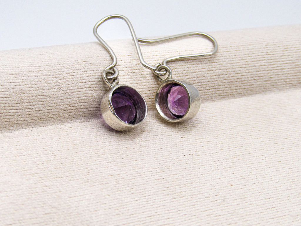 Silver earrings with purple gemstones on a beige ribbon