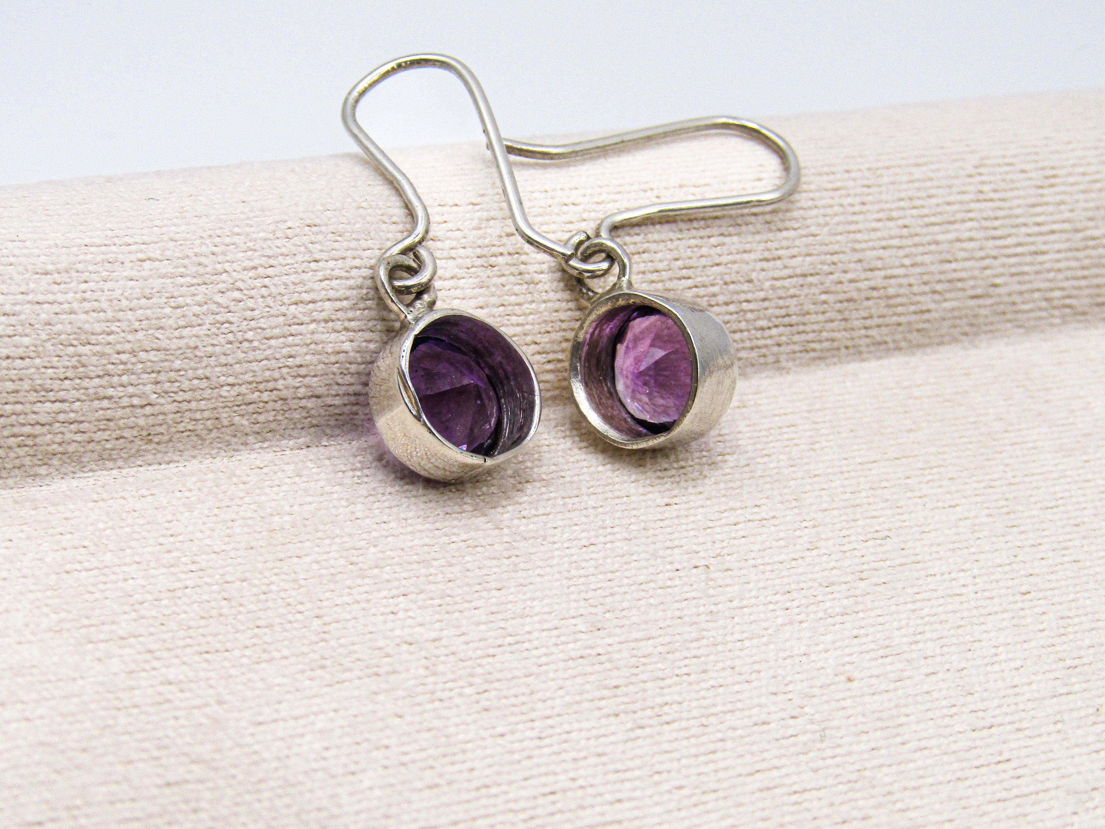 Silver earrings with purple gemstones on a beige ribbon
