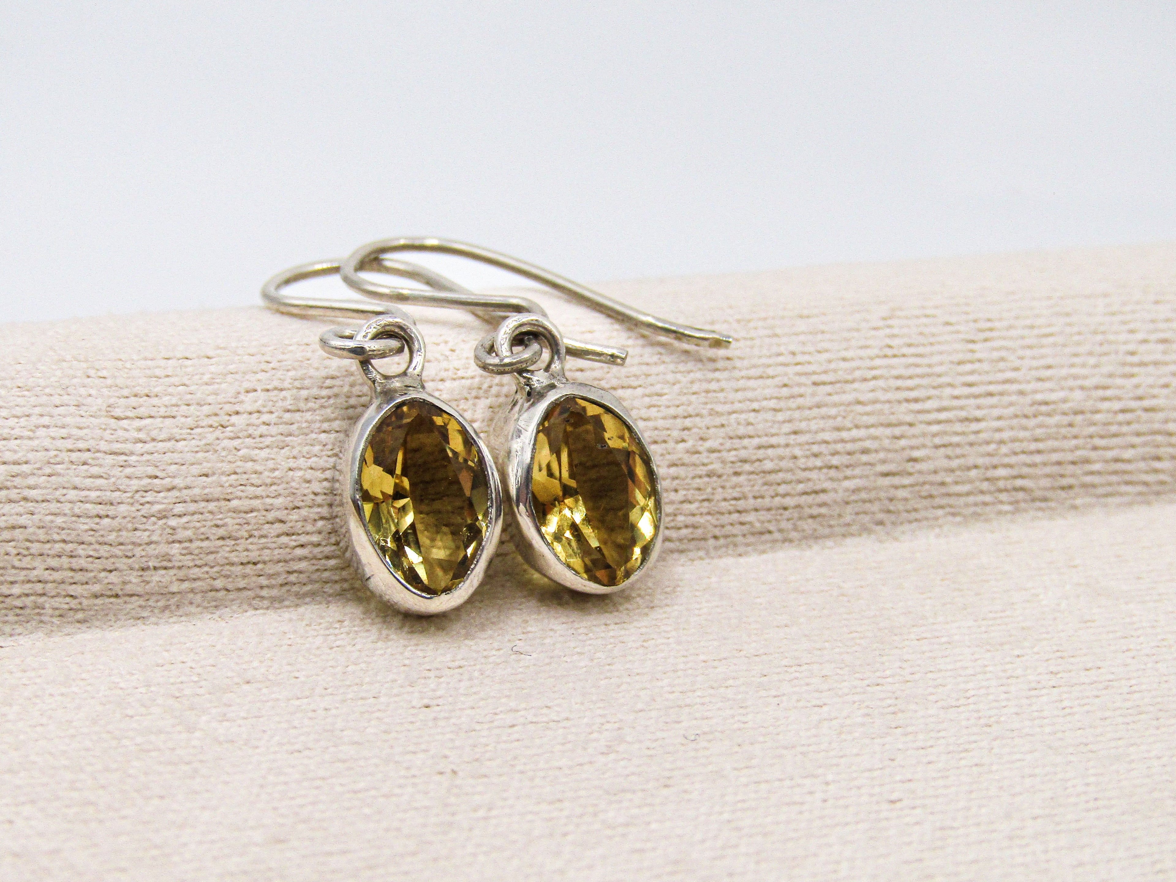 Pair of silver earrings with yellow gemstones on a beige fabric background