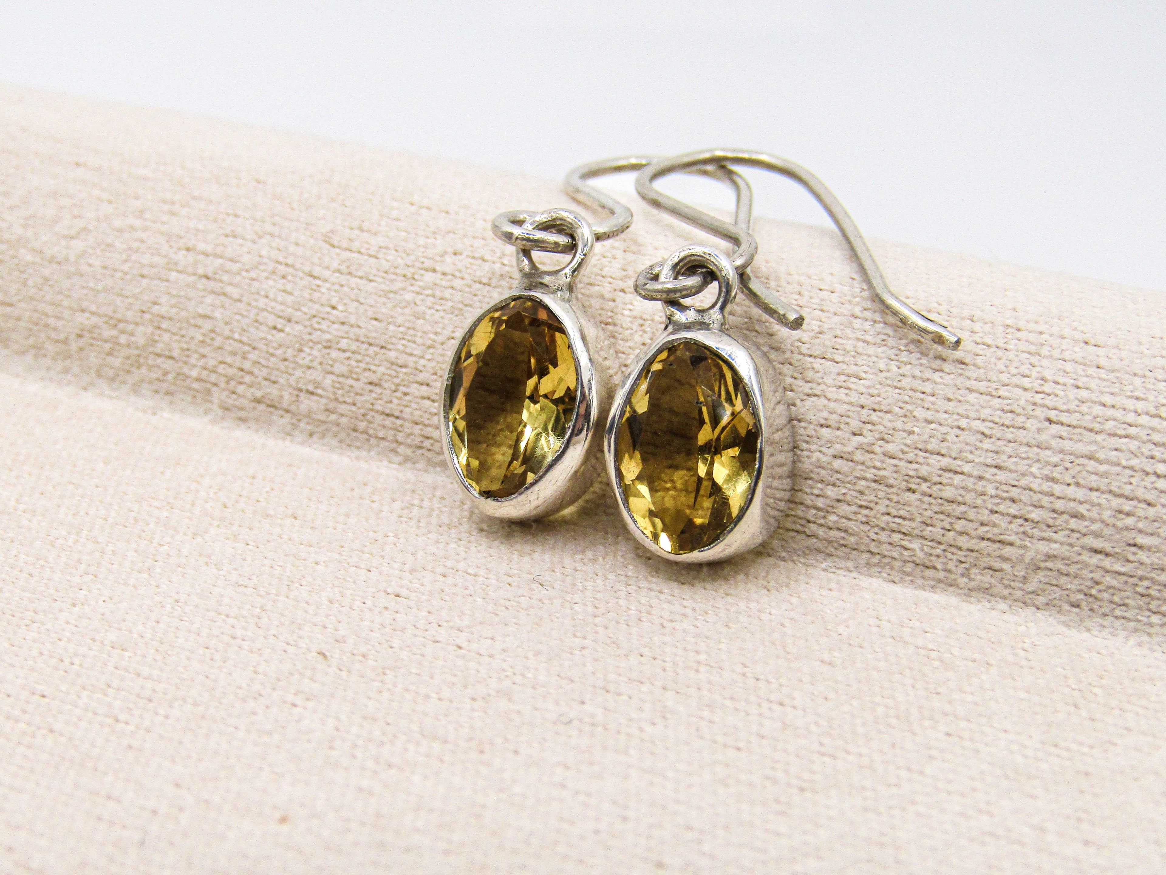 Pair of silver earrings with yellow gemstones on a beige fabric background