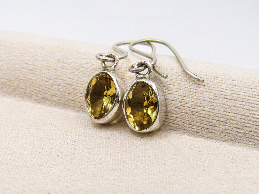 Silver earrings with yellow gemstones on a beige fabric background