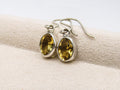 Silver earrings with yellow gemstones on a beige fabric background