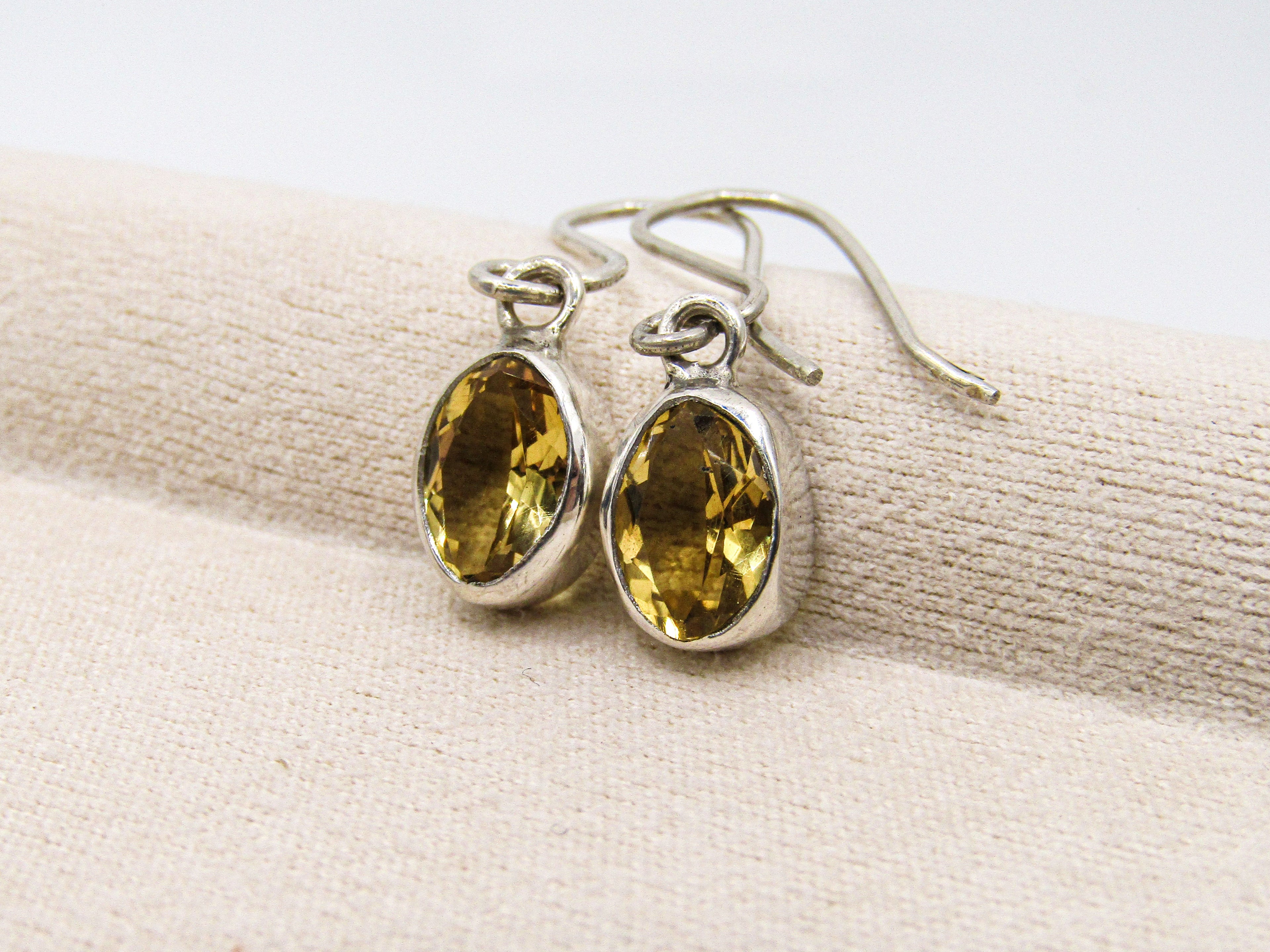 Silver earrings with yellow gemstones on a beige fabric background