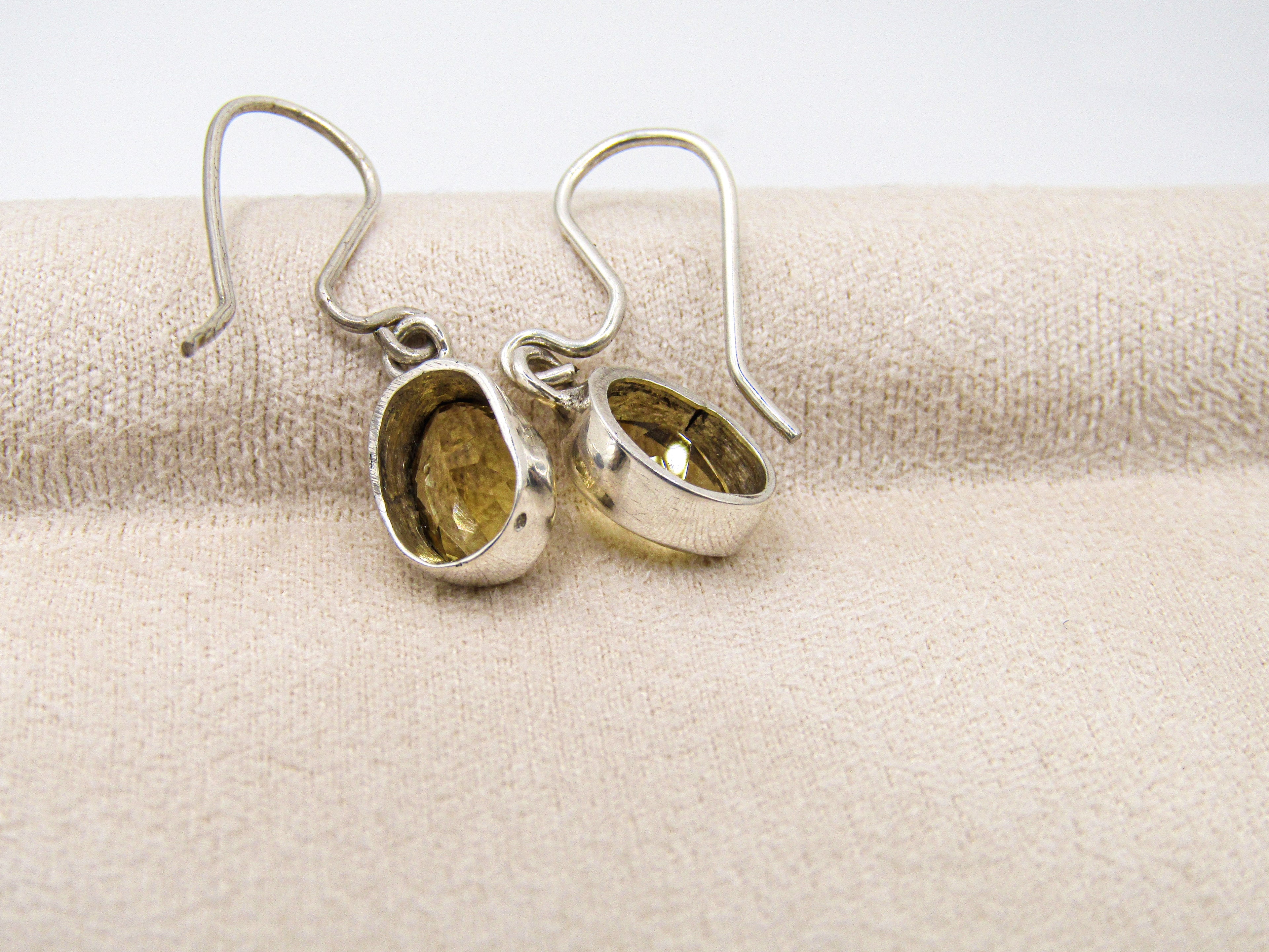 Silver earrings with embedded stones on a beige fabric background