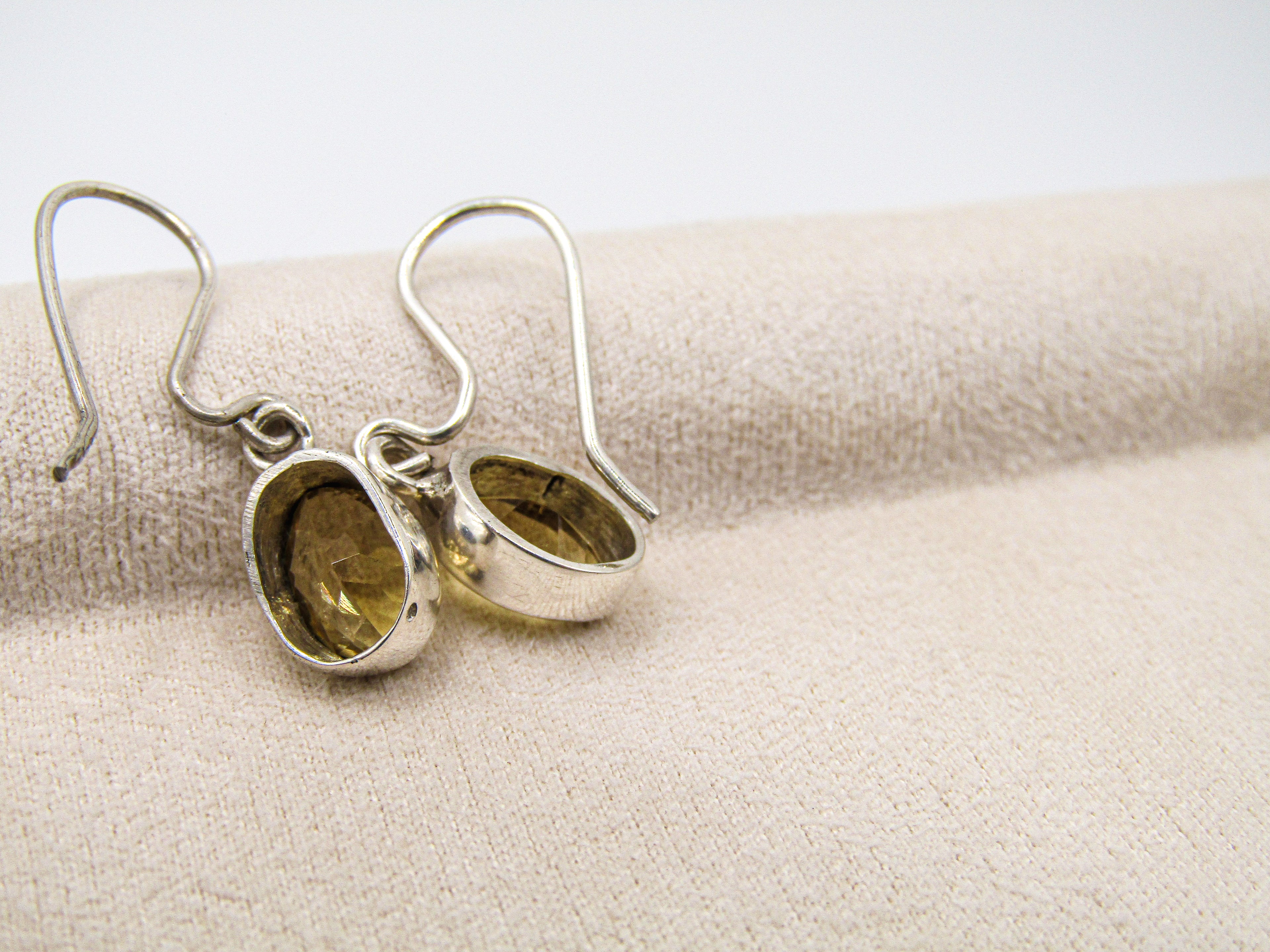 Silver earrings with embedded stones on a beige fabric background