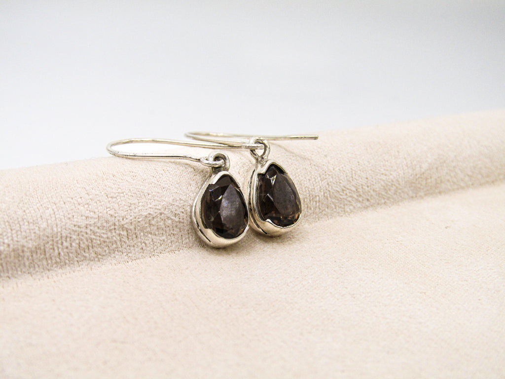 Pair of silver earrings with black stones on a beige fabric background