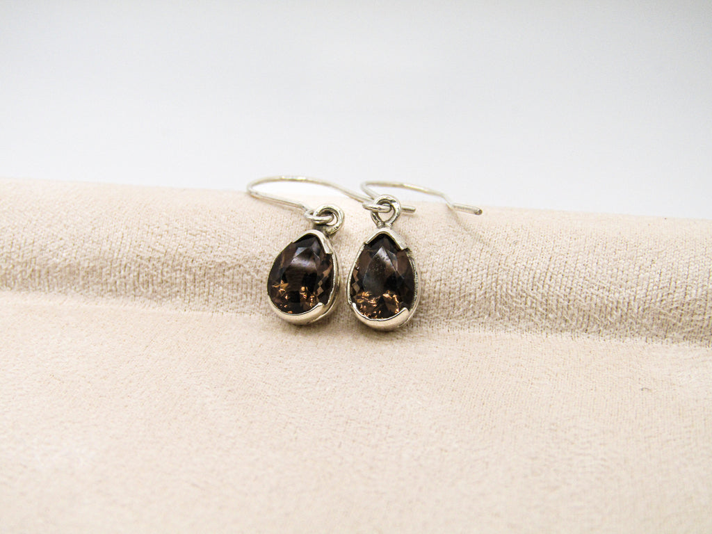 Teardrop-shaped earrings with dark stones on a beige fabric background