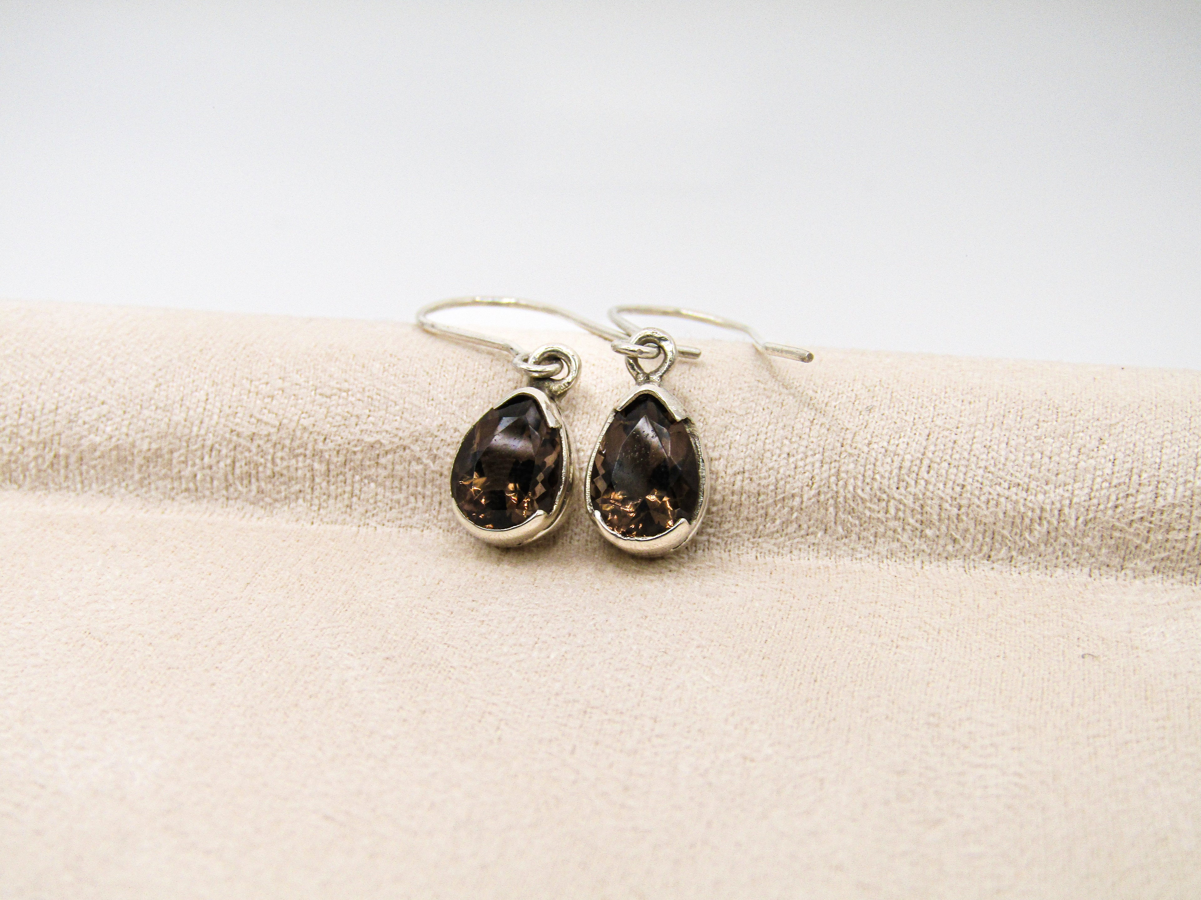 Teardrop-shaped earrings with dark stones on a beige fabric background