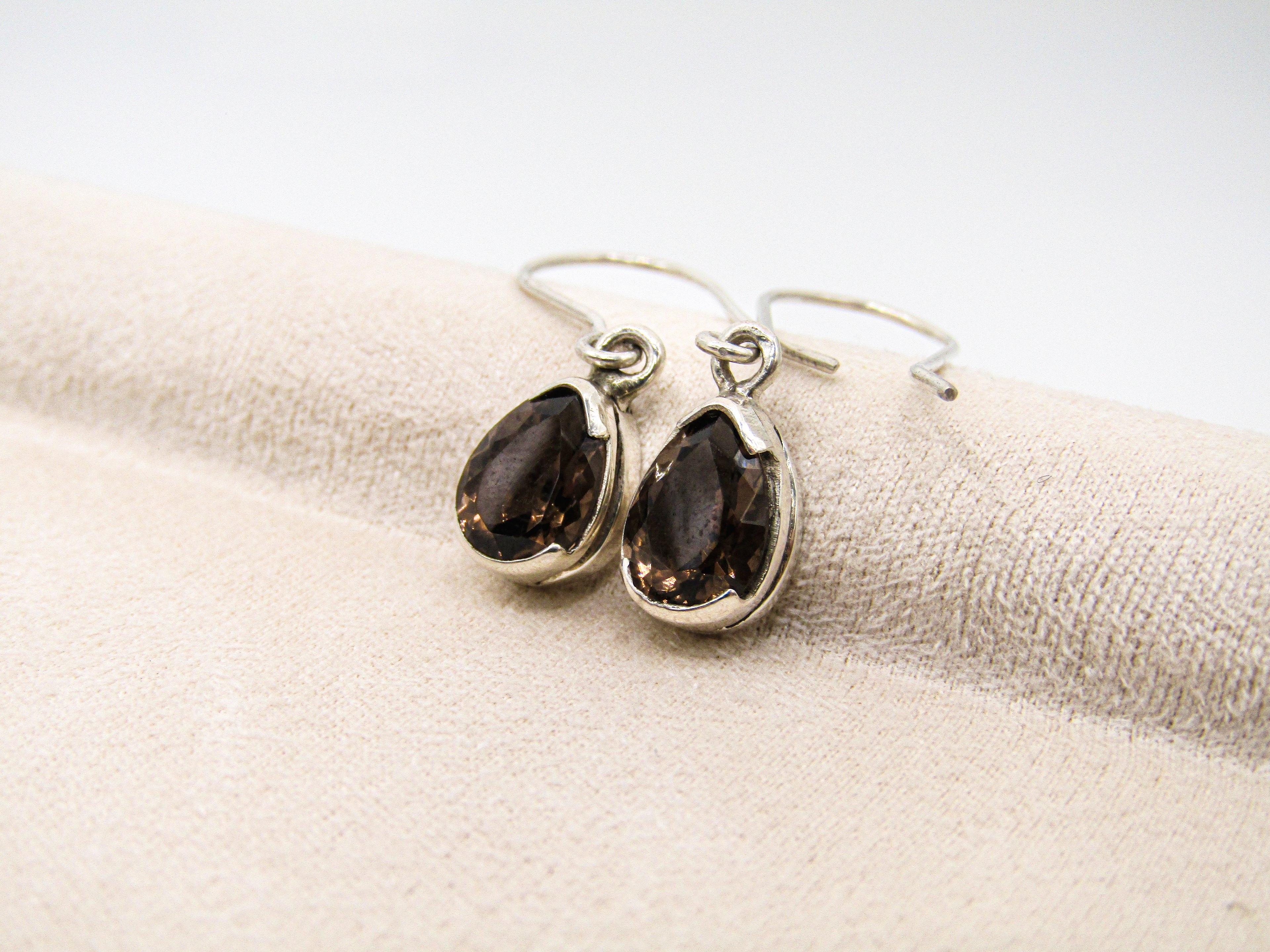 Silver earrings with dark gemstones on a beige fabric background