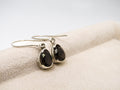 Silver earrings with black gemstones on a beige fabric background
