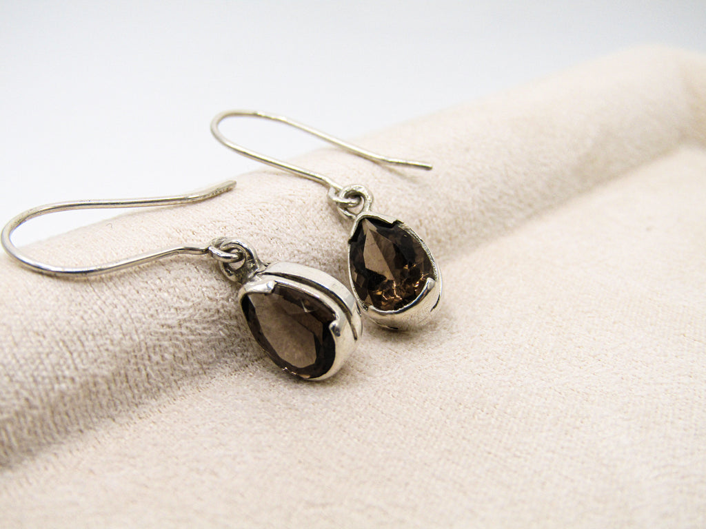 Pair of silver teardrop earrings with dark gemstones on a textured beige surface