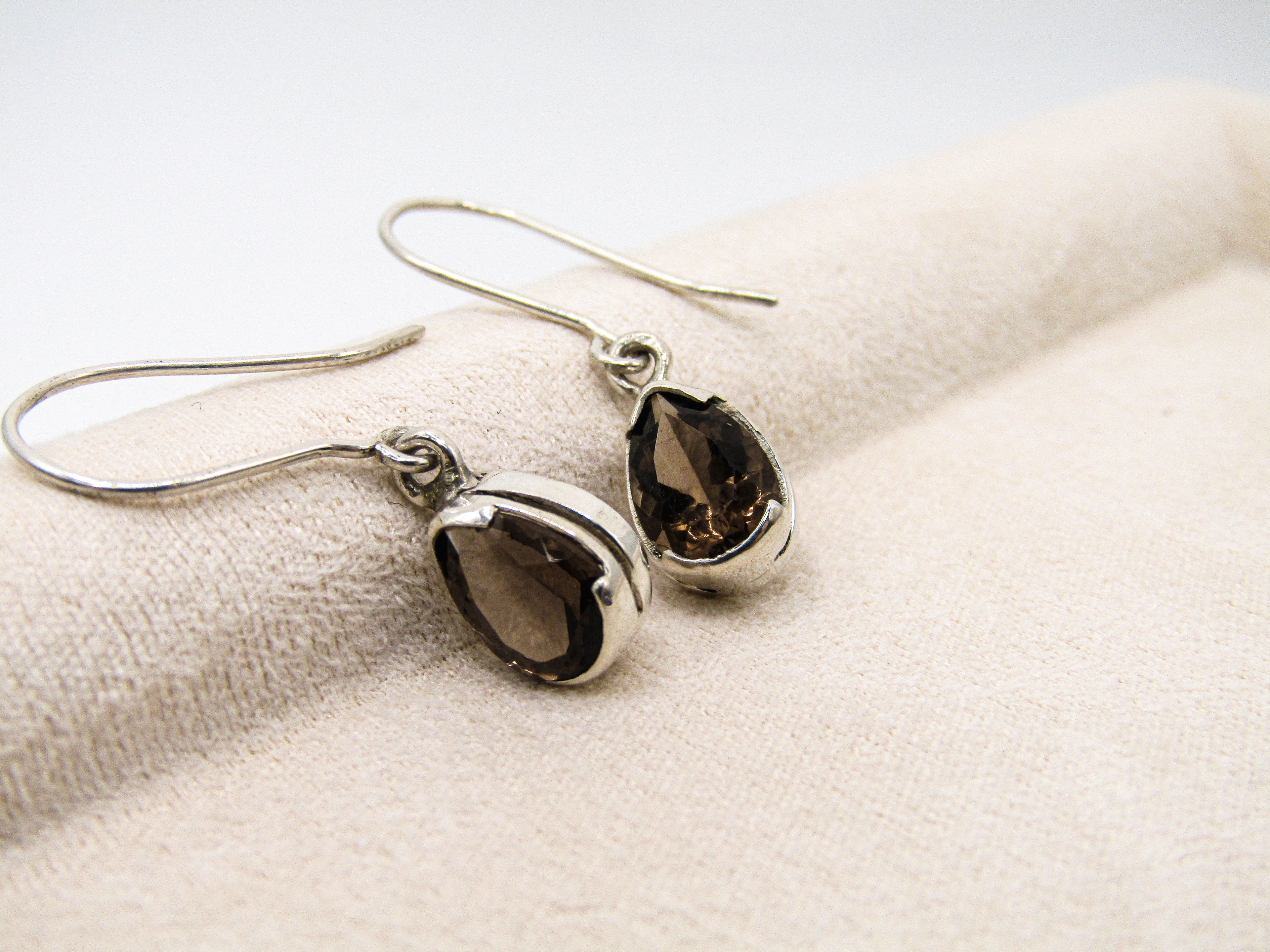 Pair of silver teardrop earrings with dark gemstones on a textured beige surface