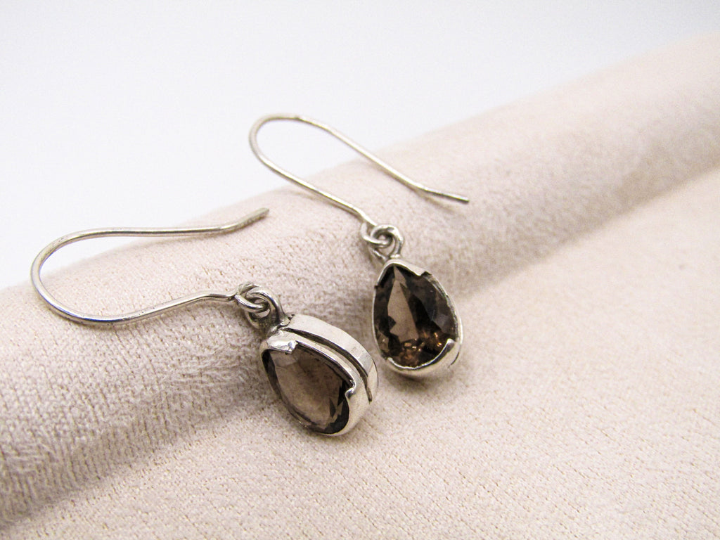 Pair of silver teardrop earrings on a beige fabric background