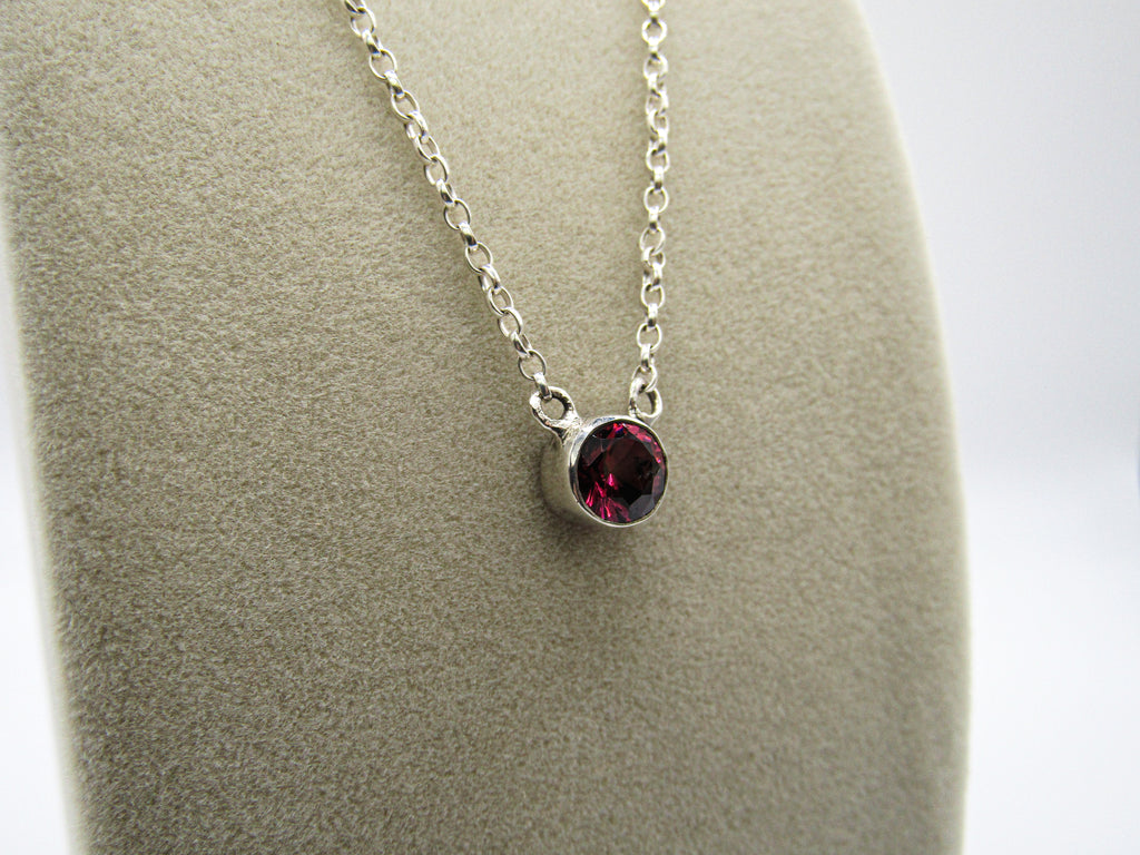 Silver necklace with a red gemstone pendant on a gray surface