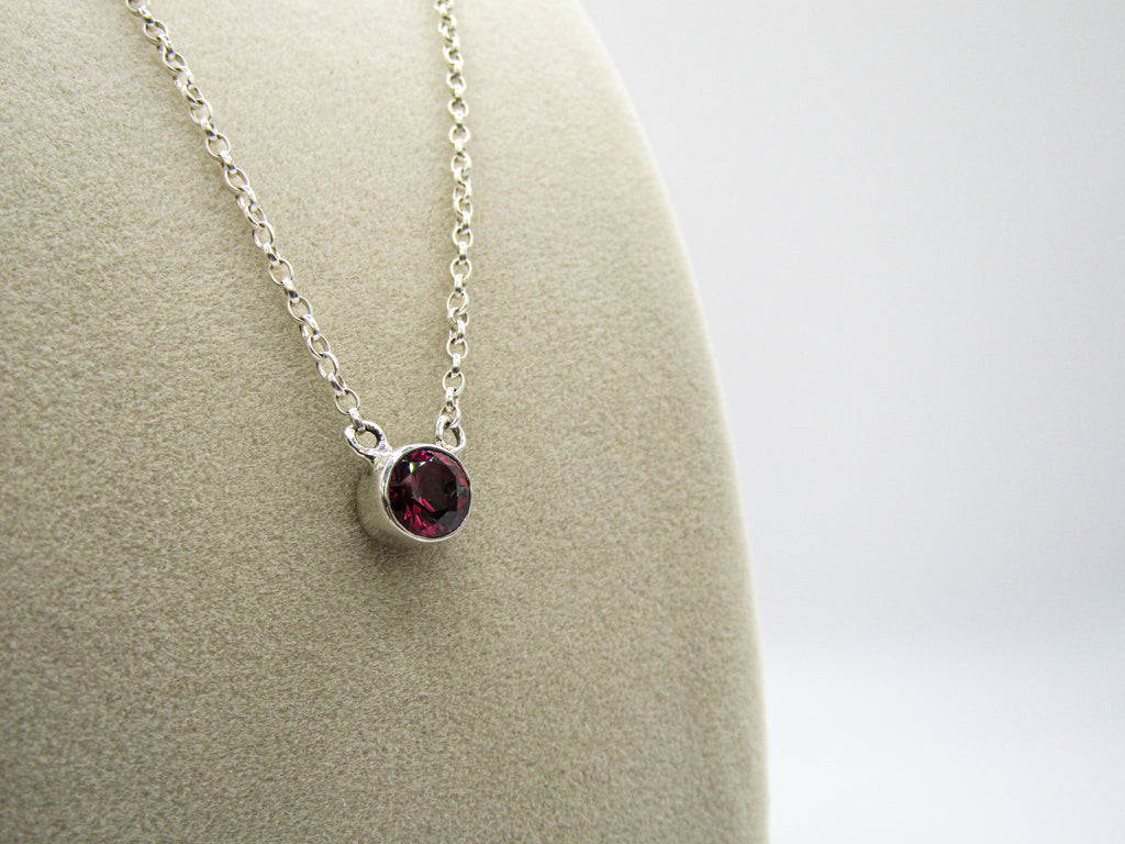 Silver necklace with a red gemstone pendant on a mannequin bust.