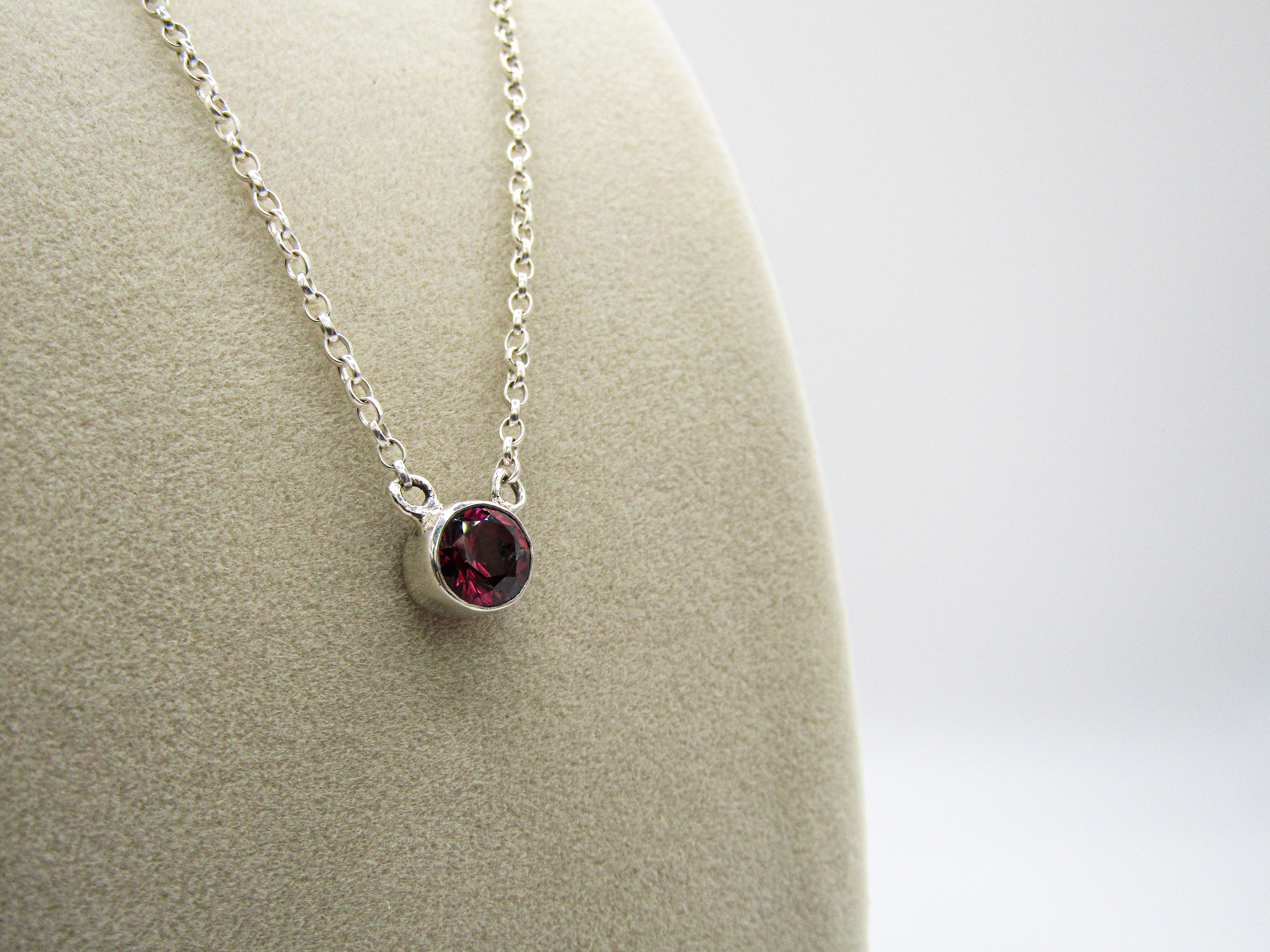 Silver necklace with a red gemstone pendant on a mannequin bust.