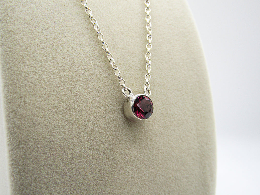 Silver necklace with a red gemstone pendant on a gray surface